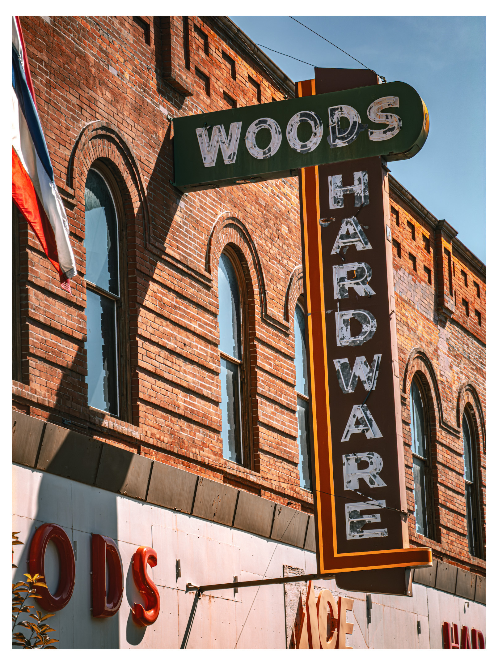 Auto-generated description: A vintage sign for Woods Hardware is mounted on a brick building with arched windows.