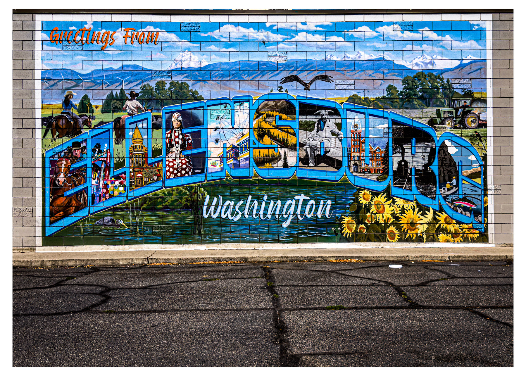 Auto-generated description: A colorful mural on a brick wall features the word Ellensburg with various artistic scenes inside the letters and includes the text Greetings From and Washington.