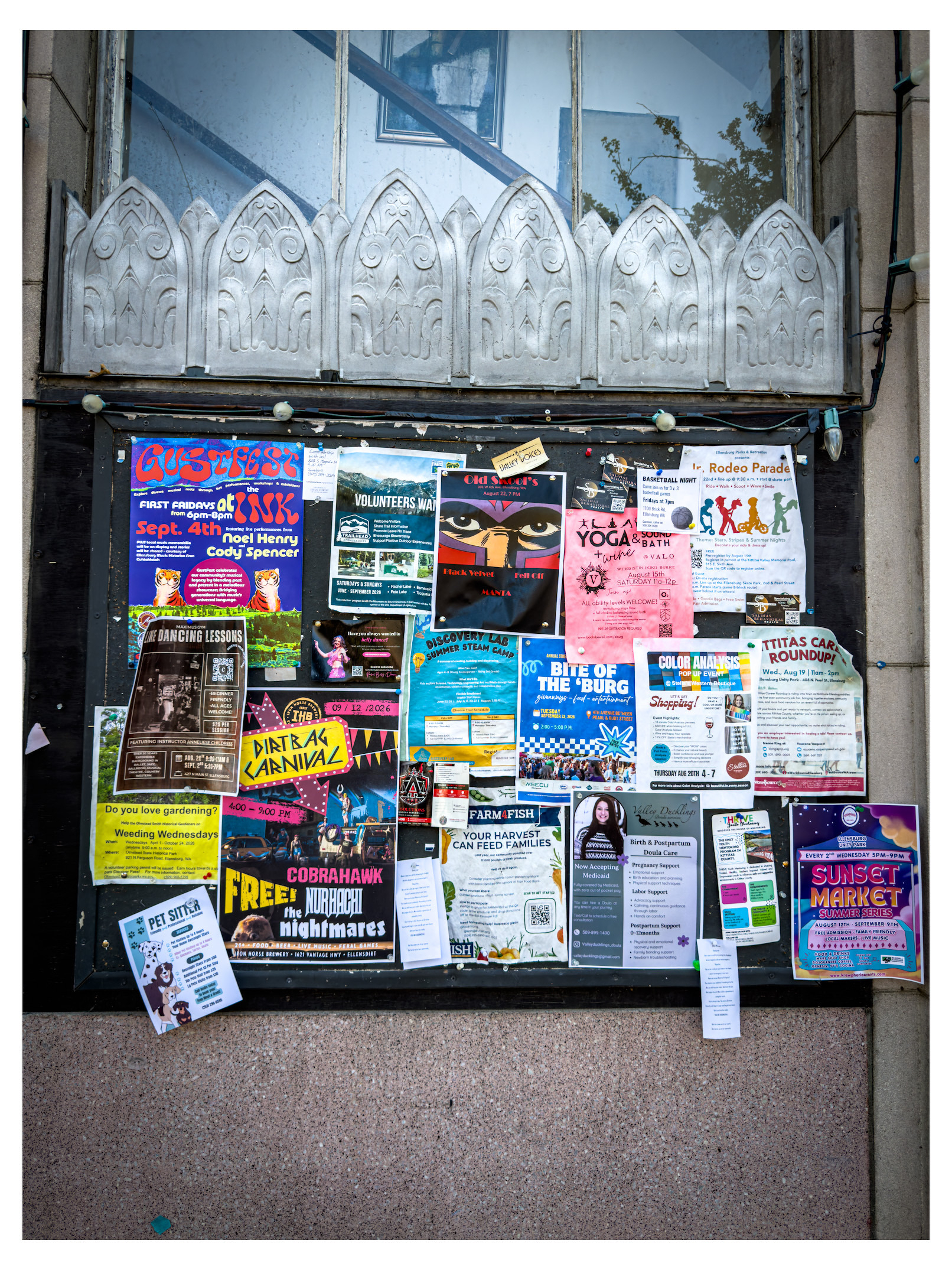 Auto-generated description: A bulletin board covered with various colorful flyers and posters advertising local events, classes, services, and announcements is displayed on a building exterior.