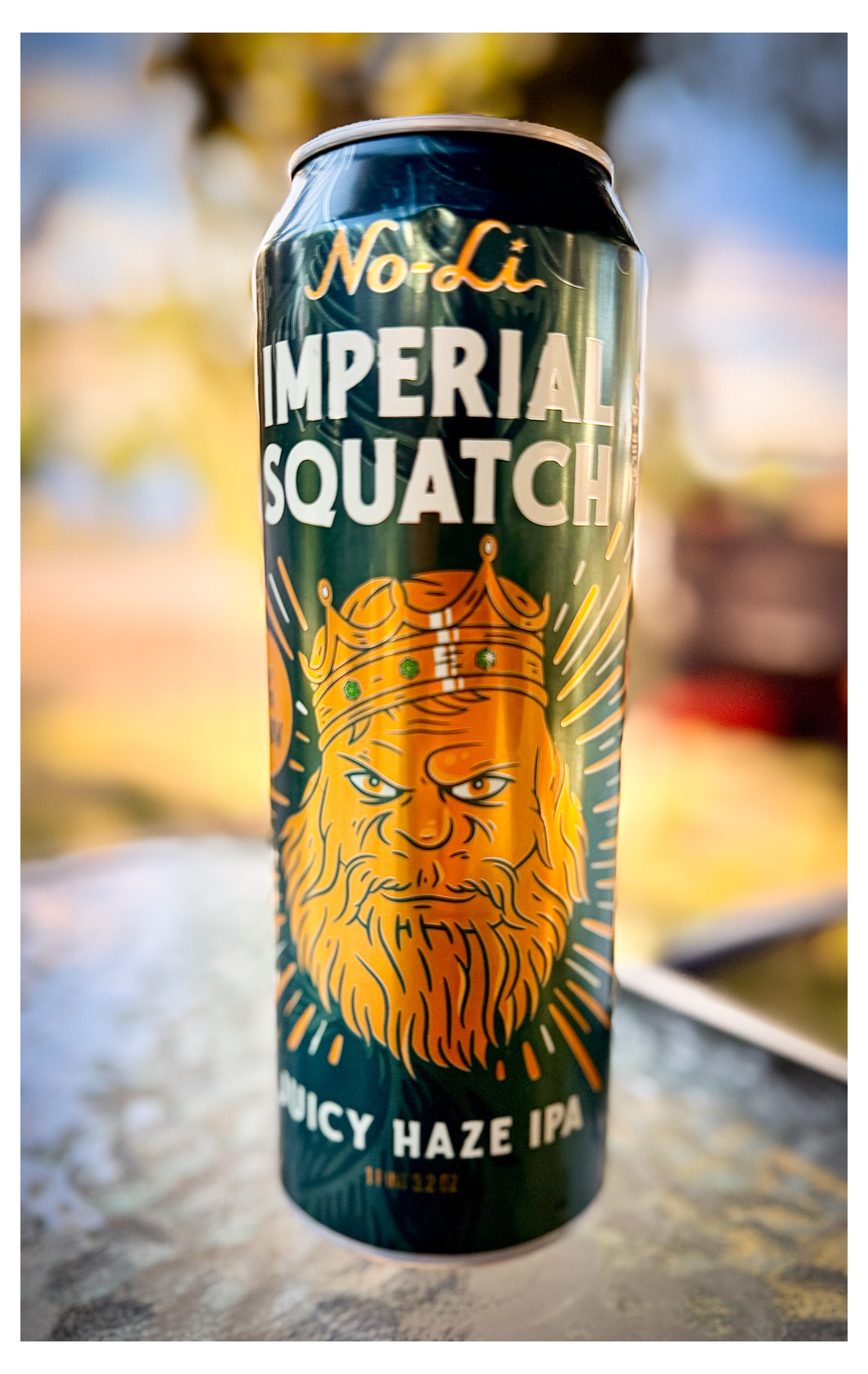Auto-generated description: A can of No-Li Imperial Squatch Juicy Haze IPA with an illustrated bearded king wearing a crown is pictured on a glass surface.
