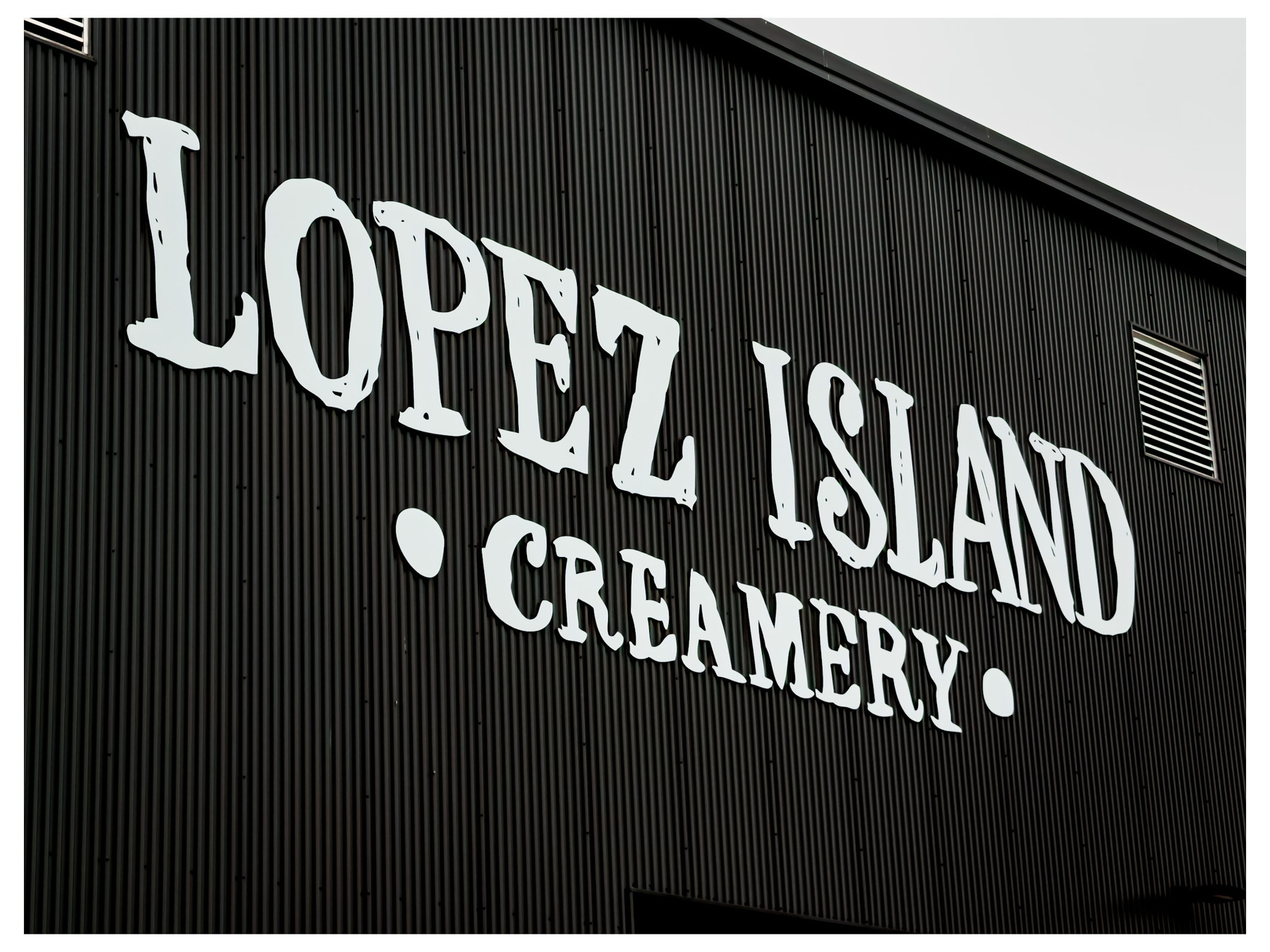 Auto-generated description: A black corrugated wall features large white letters spelling out Lopez Island Creamery.