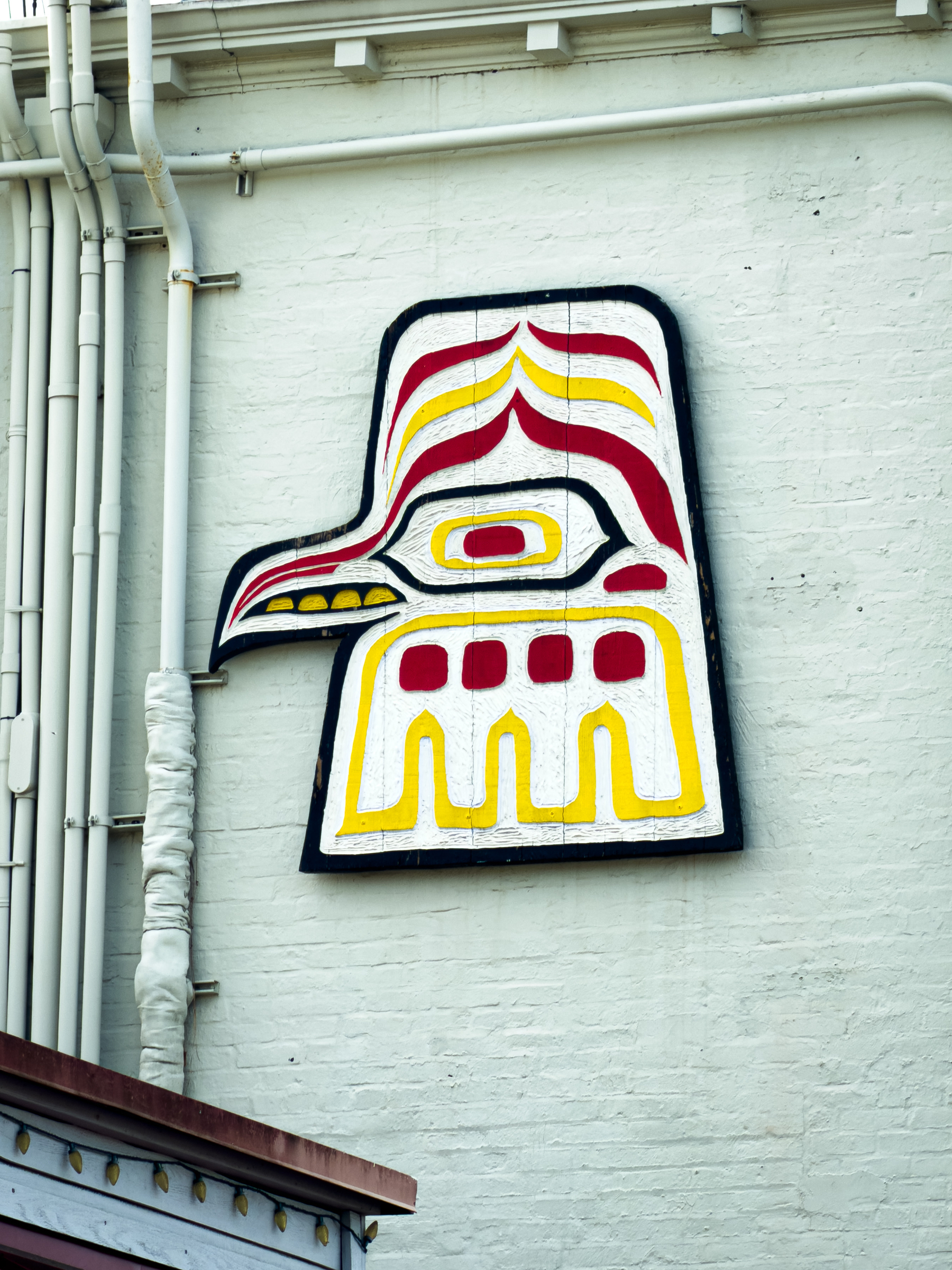 Auto-generated description: A stylized, colorful mural resembling a bird's head is painted on a white brick wall next to several vertical pipes.