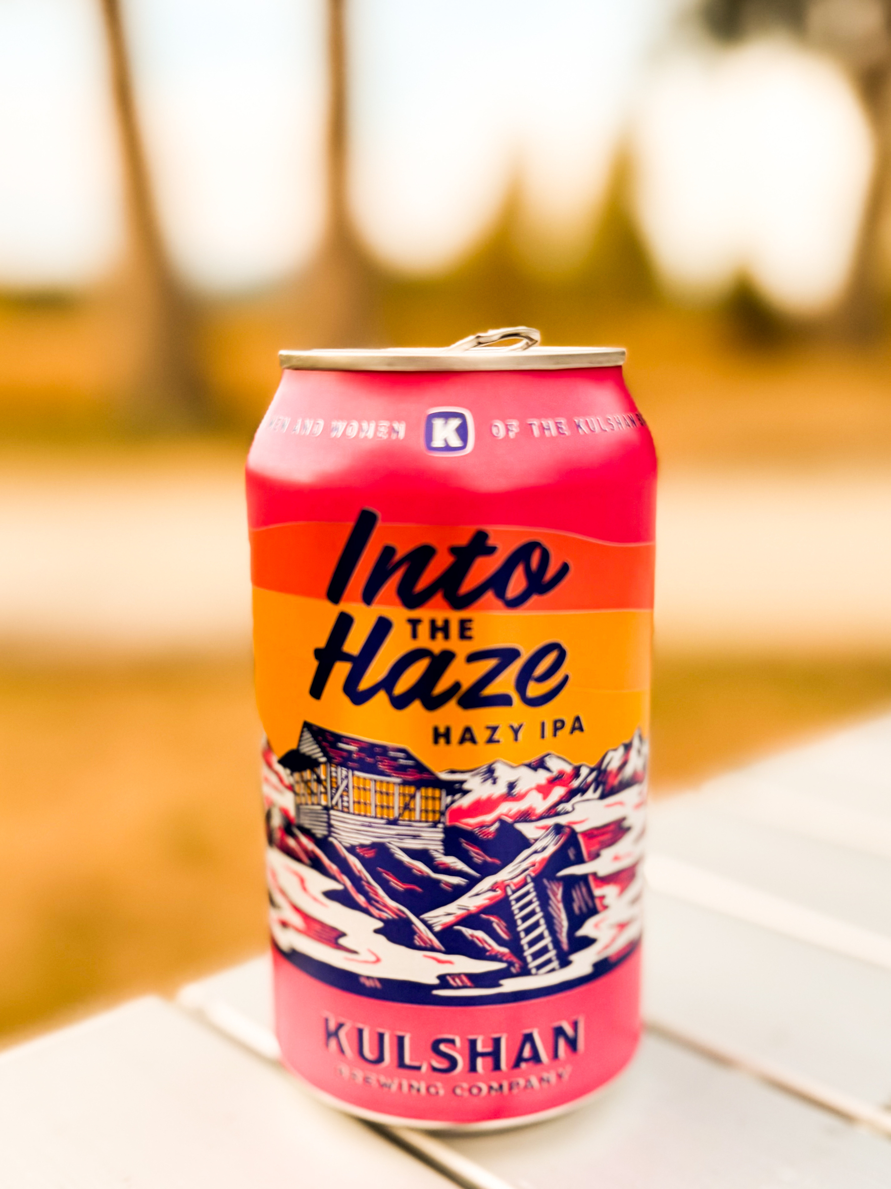 Auto-generated description: A can of Into the Haze Hazy IPA beer from Kulshan Brewing Company is placed on a white surface with a blurred outdoor background.