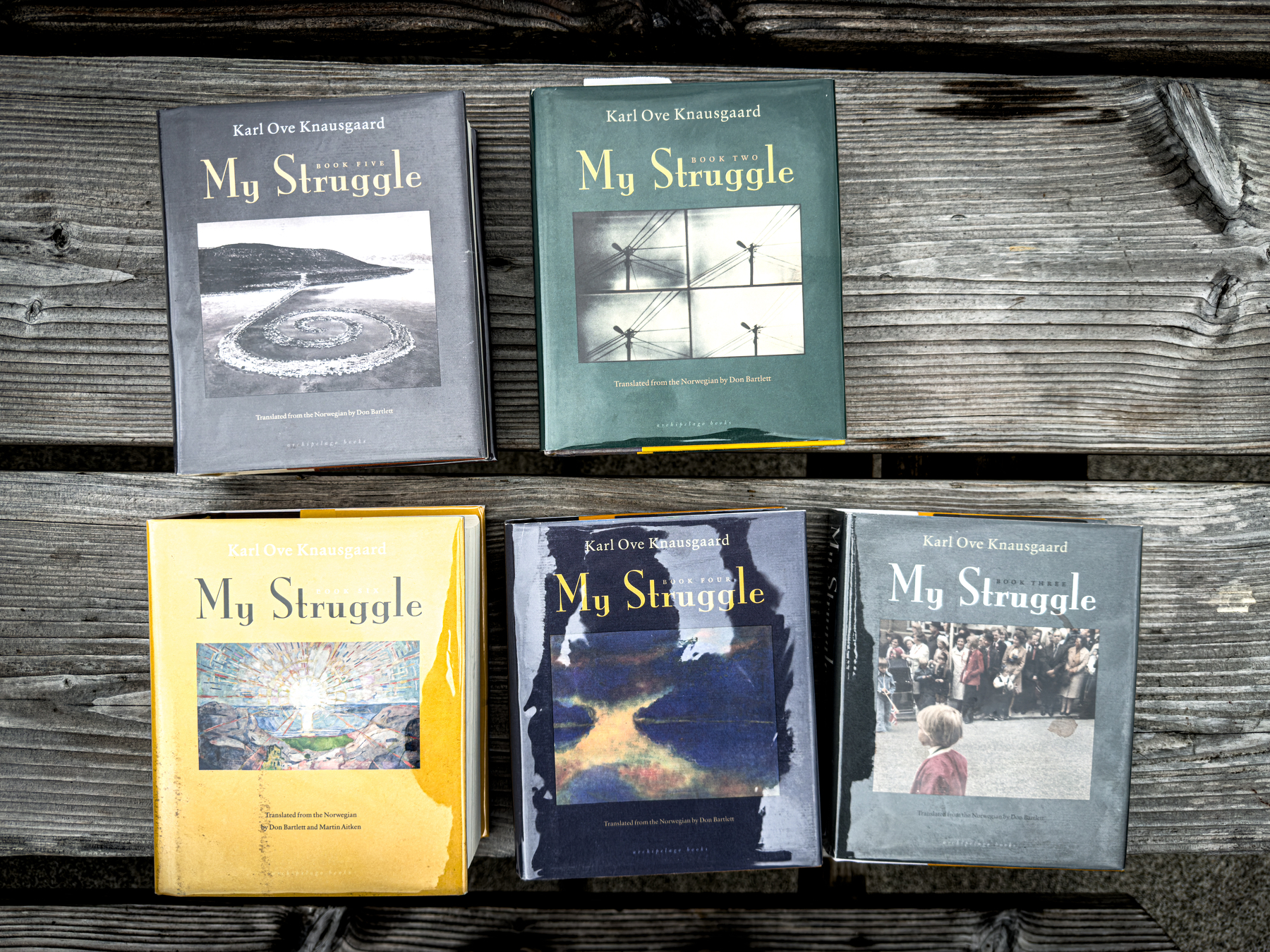 Auto-generated description: Five volumes of Karl Ove Knausgaard's book series My Struggle are arranged on a wooden surface.