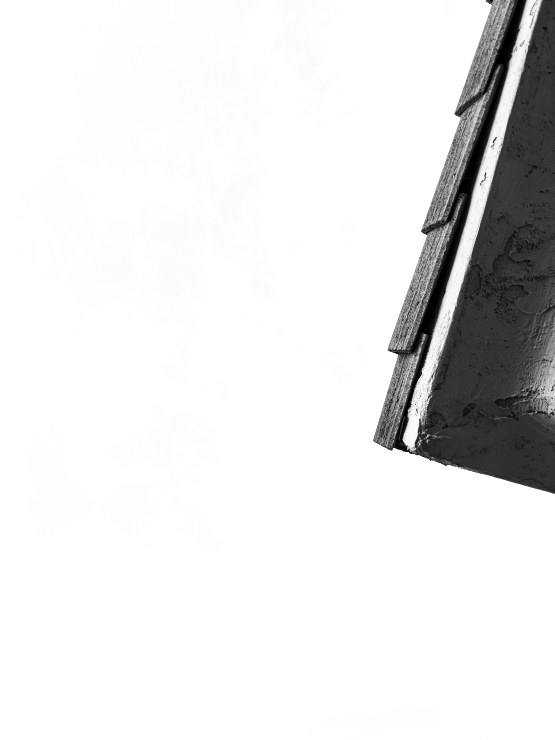 Auto-generated description: A close-up of a corner of a roof with visible shingles and textured surface against a plain white background.