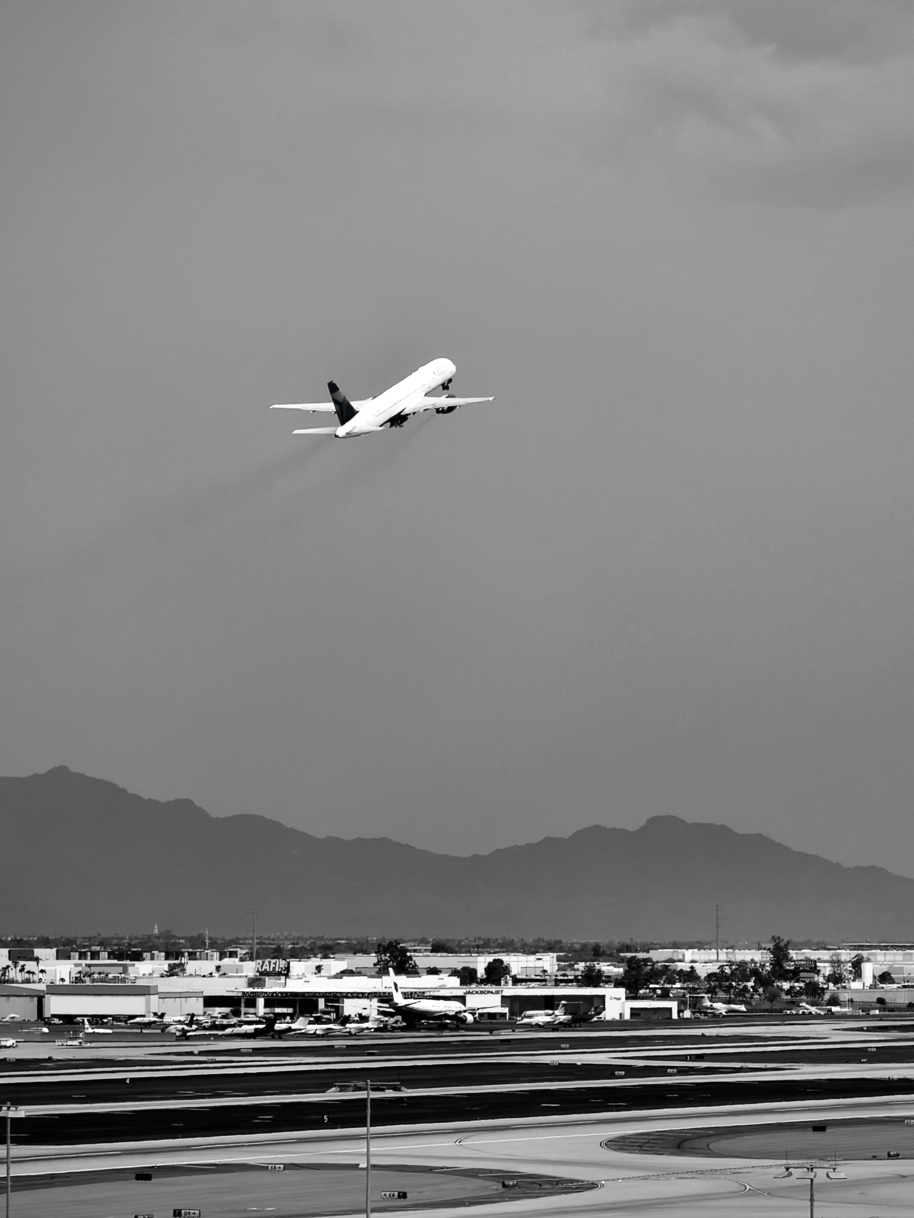 Auto-generated description: An airplane is ascending into the sky above an airport runway with mountains in the background.