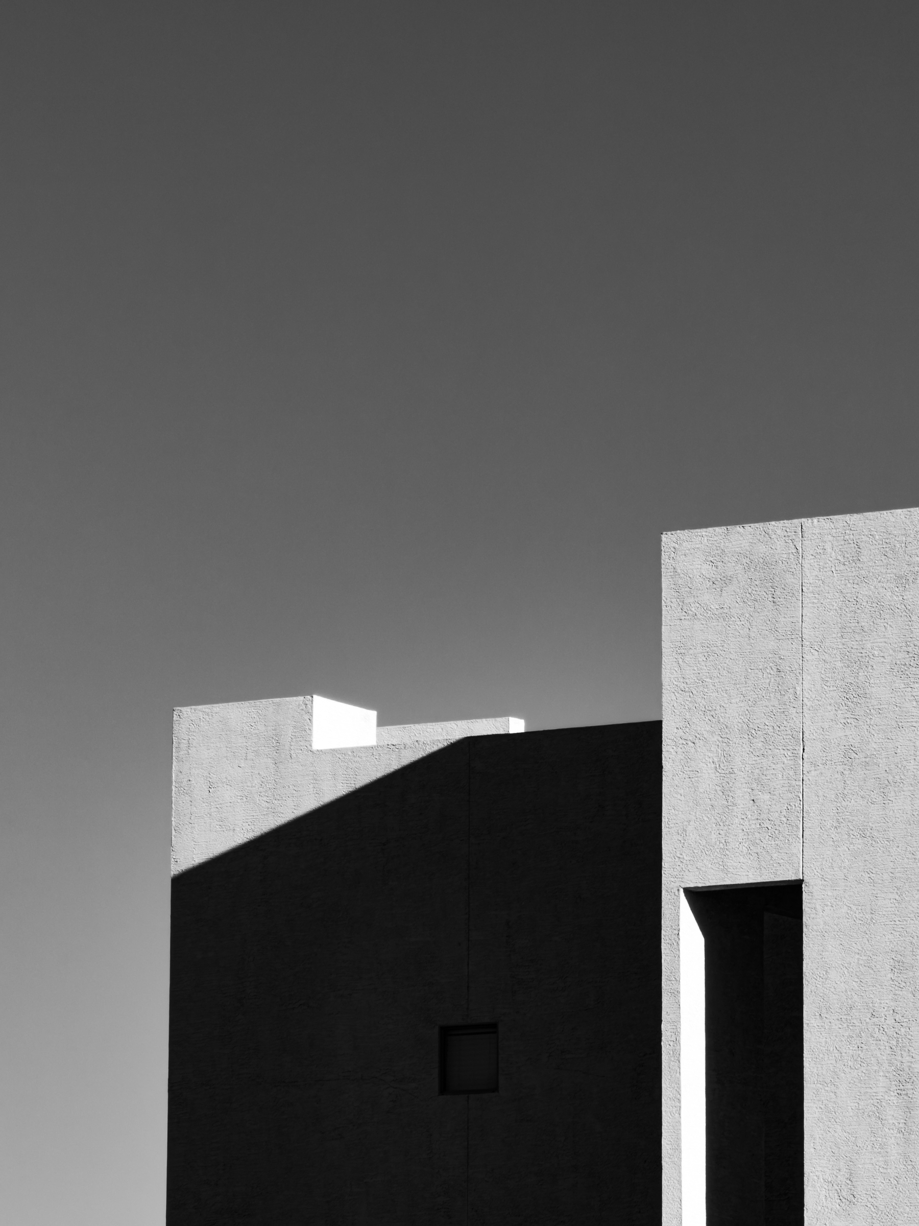 Auto-generated description: A minimalist architectural composition featuring contrasting light and shadow on a modern building under a clear sky.