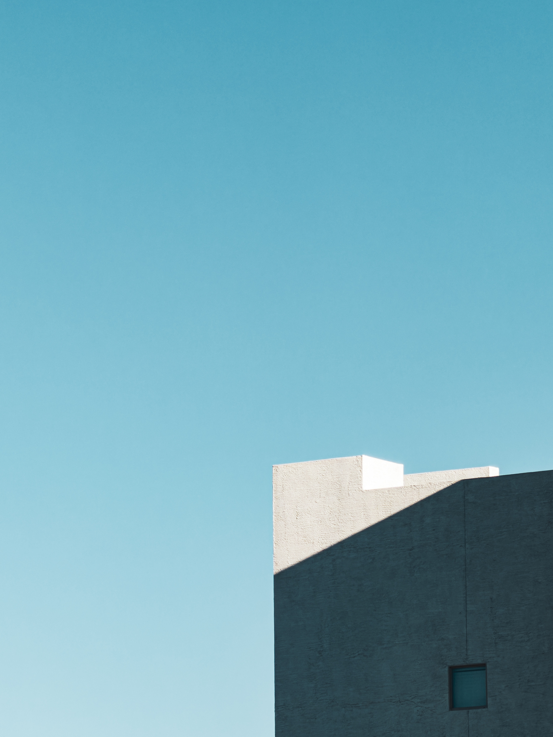 Auto-generated description: A minimalist building partially casts a shadow against a clear blue sky.