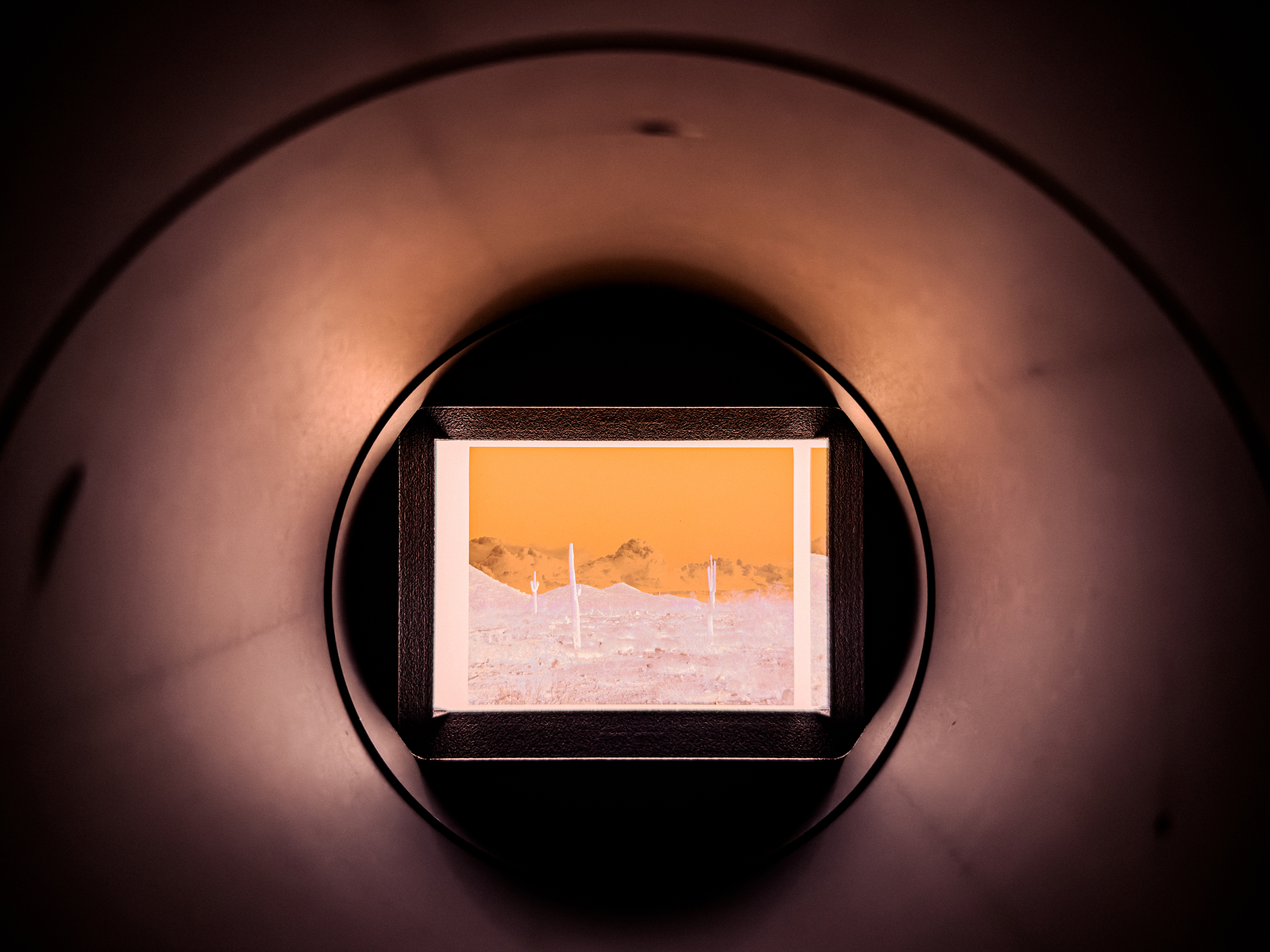 Auto-generated description: A view of a mountainous landscape with a reddish sky is seen through a circular tunnel or pipe, framing the scene like a window.