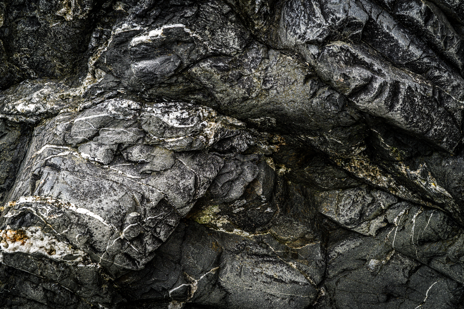 Auto-generated description: Dark, textured volcanic rock formations with visible cracks and layers dominate the scene.