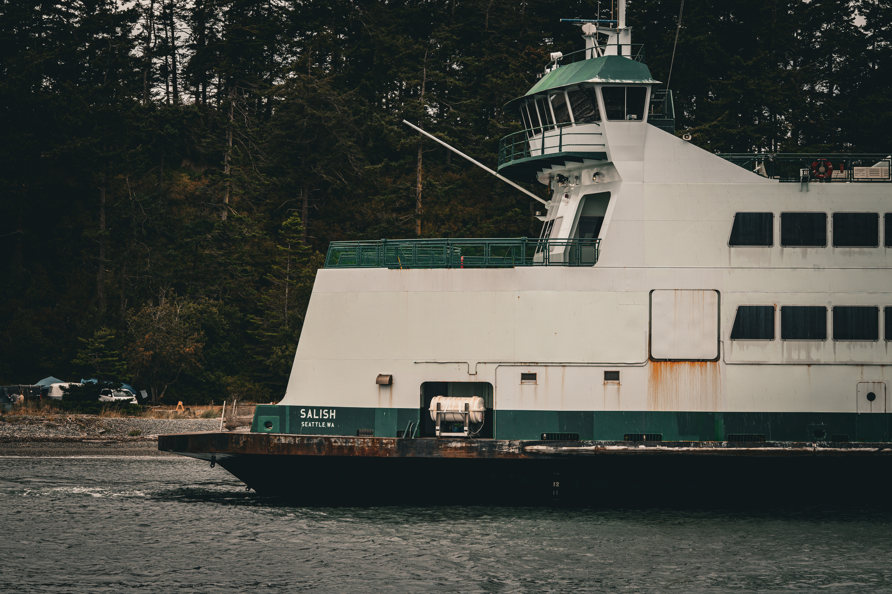 Auto-generated description: A large ferry named Salish is cruising on the water near a forested shoreline.