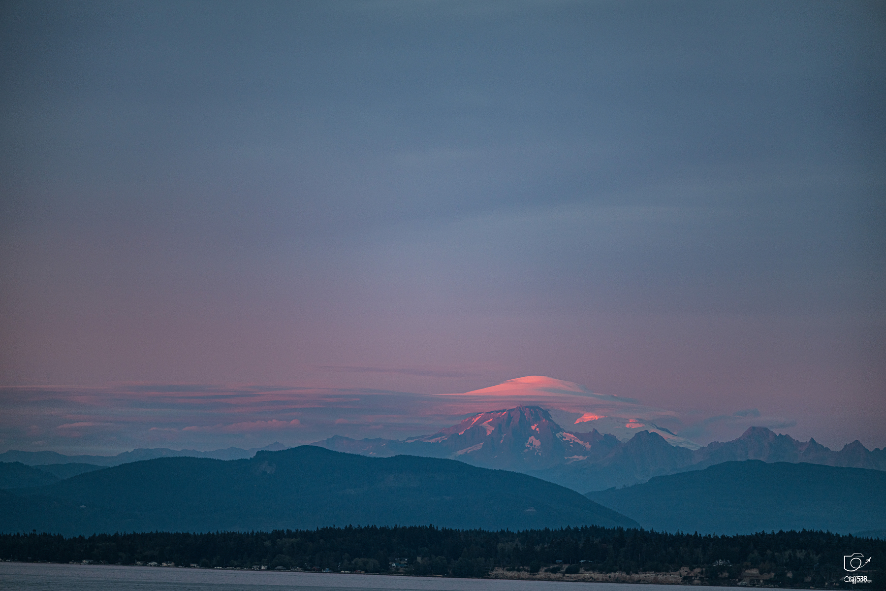 Auto-generated description: A serene landscape features distant mountains illuminated by soft pink and purple hues under a calm sky.