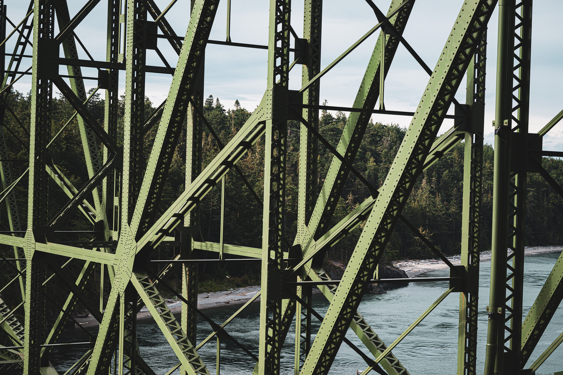 Auto-generated description: A green metal truss bridge spans over a river with trees visible in the background.