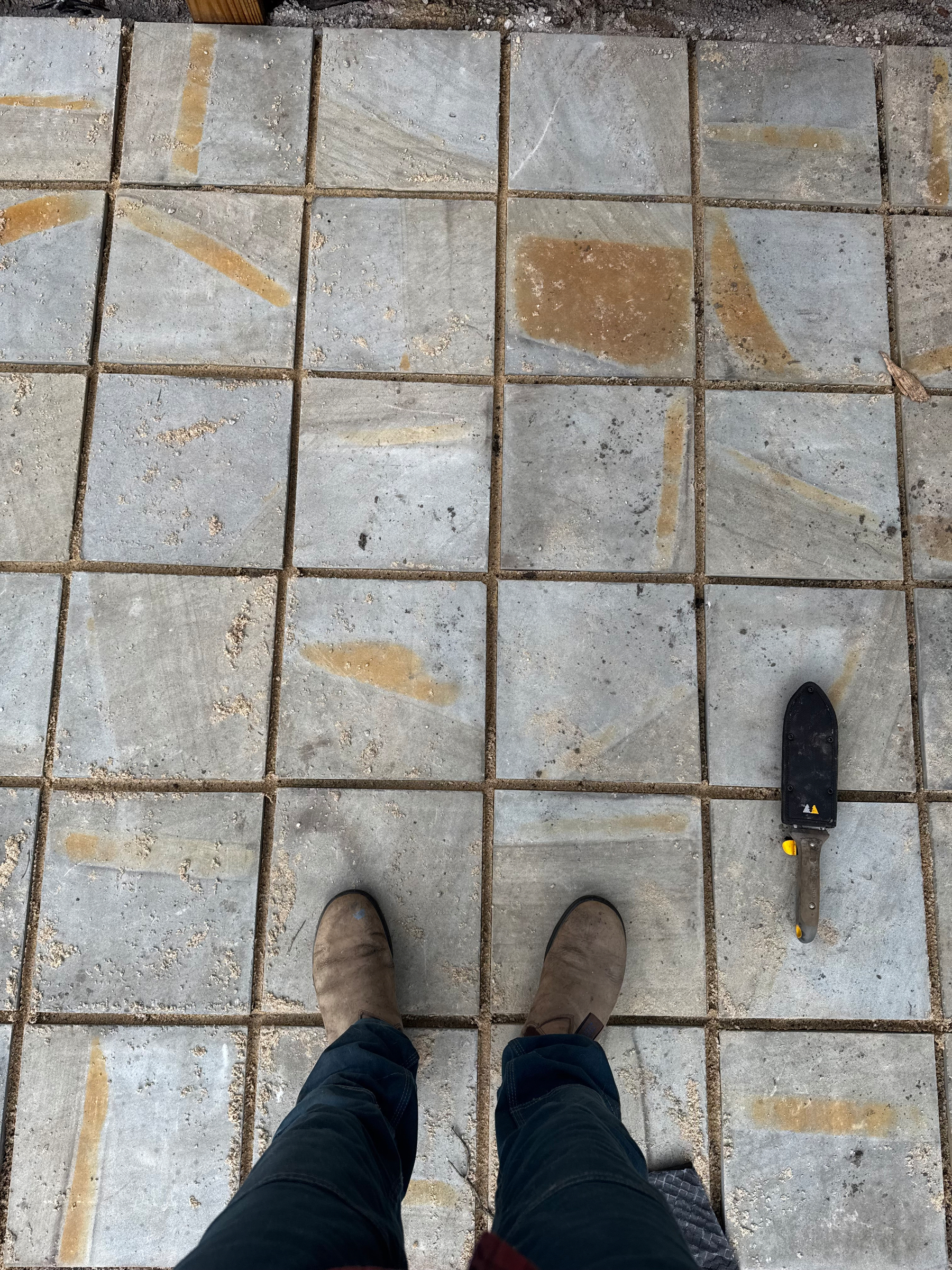 Tiles are being laid on the ground, with a trowel nearby and someone's feet visible.