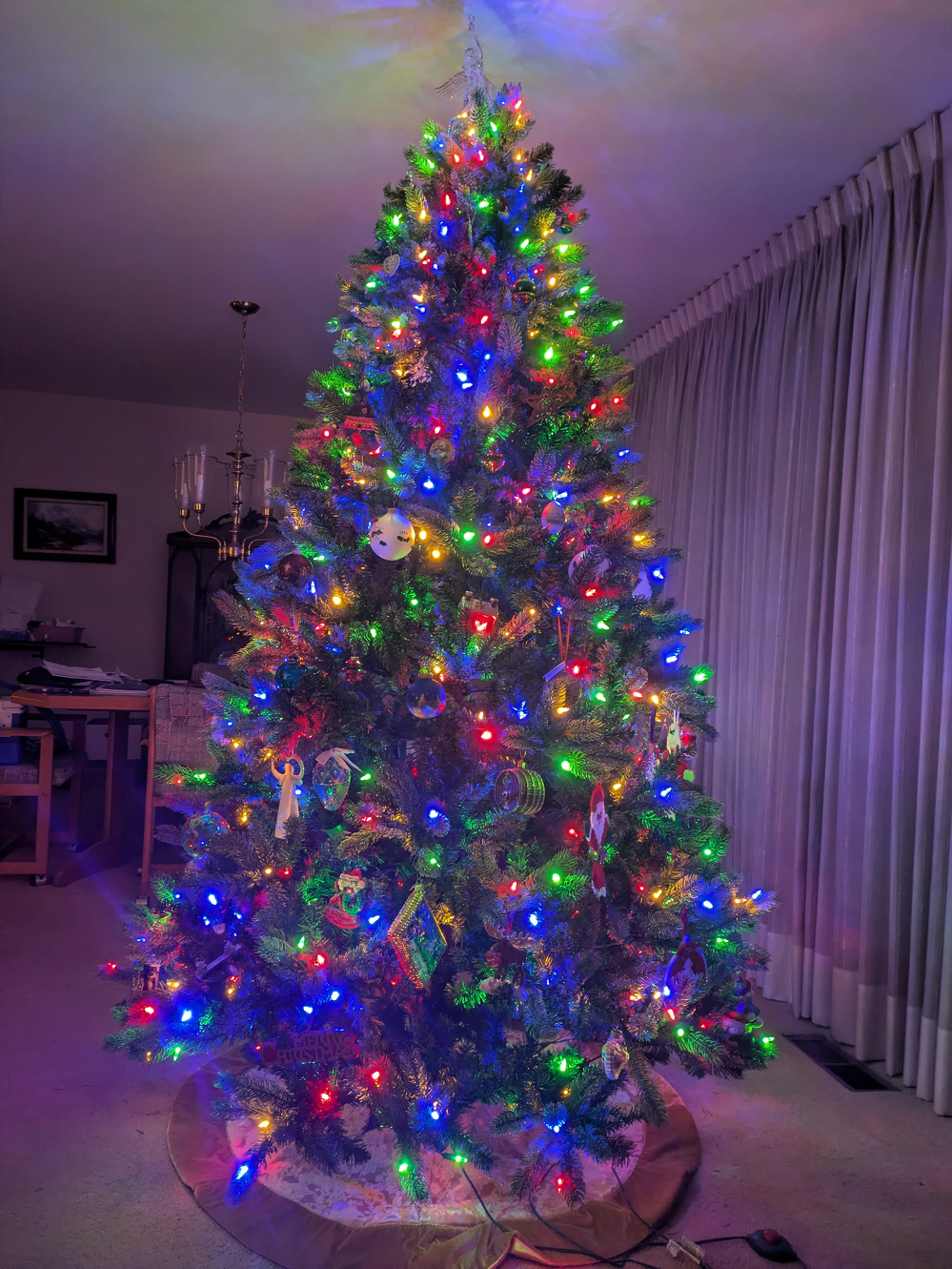 A beautifully decorated Christmas tree is adorned with colorful lights and ornaments, standing in a cozy living room.
