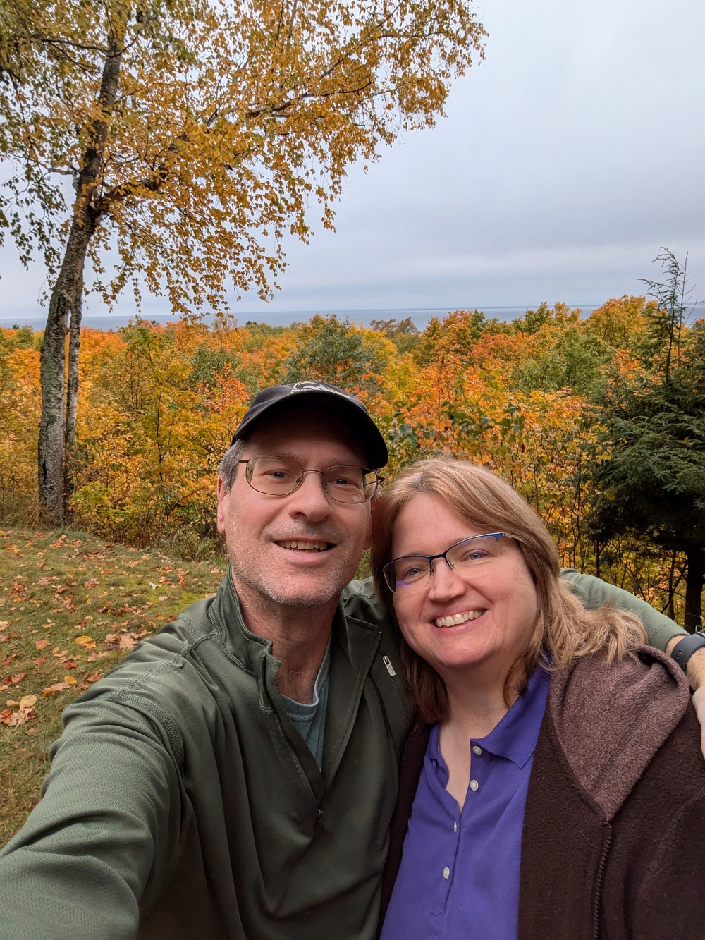 A couple is taking a selfie in front of a scenic view of autumn trees.