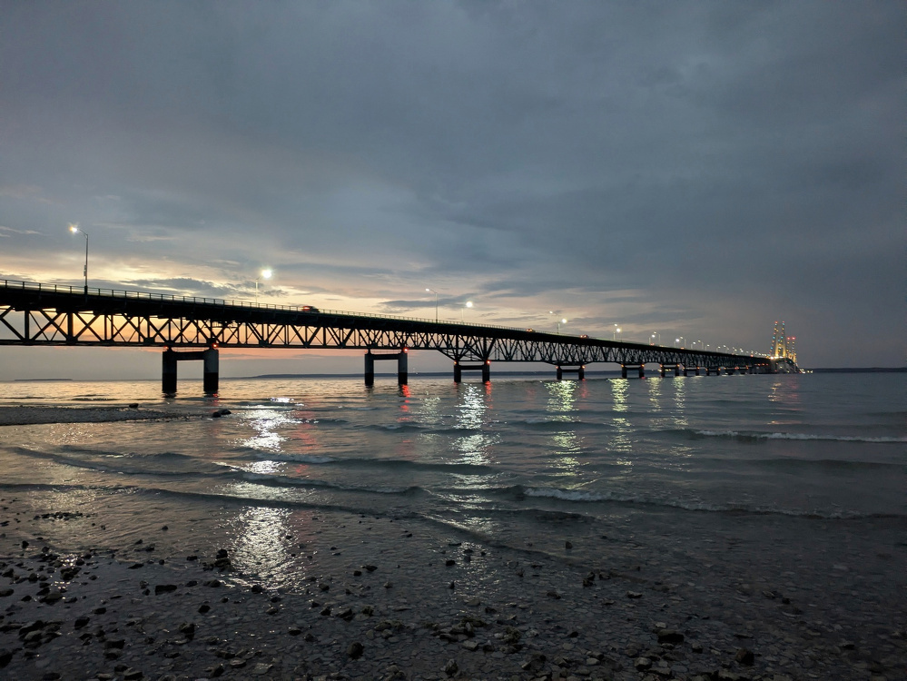 A long bridge stretches across a body of water under a cloudy, evening sky.