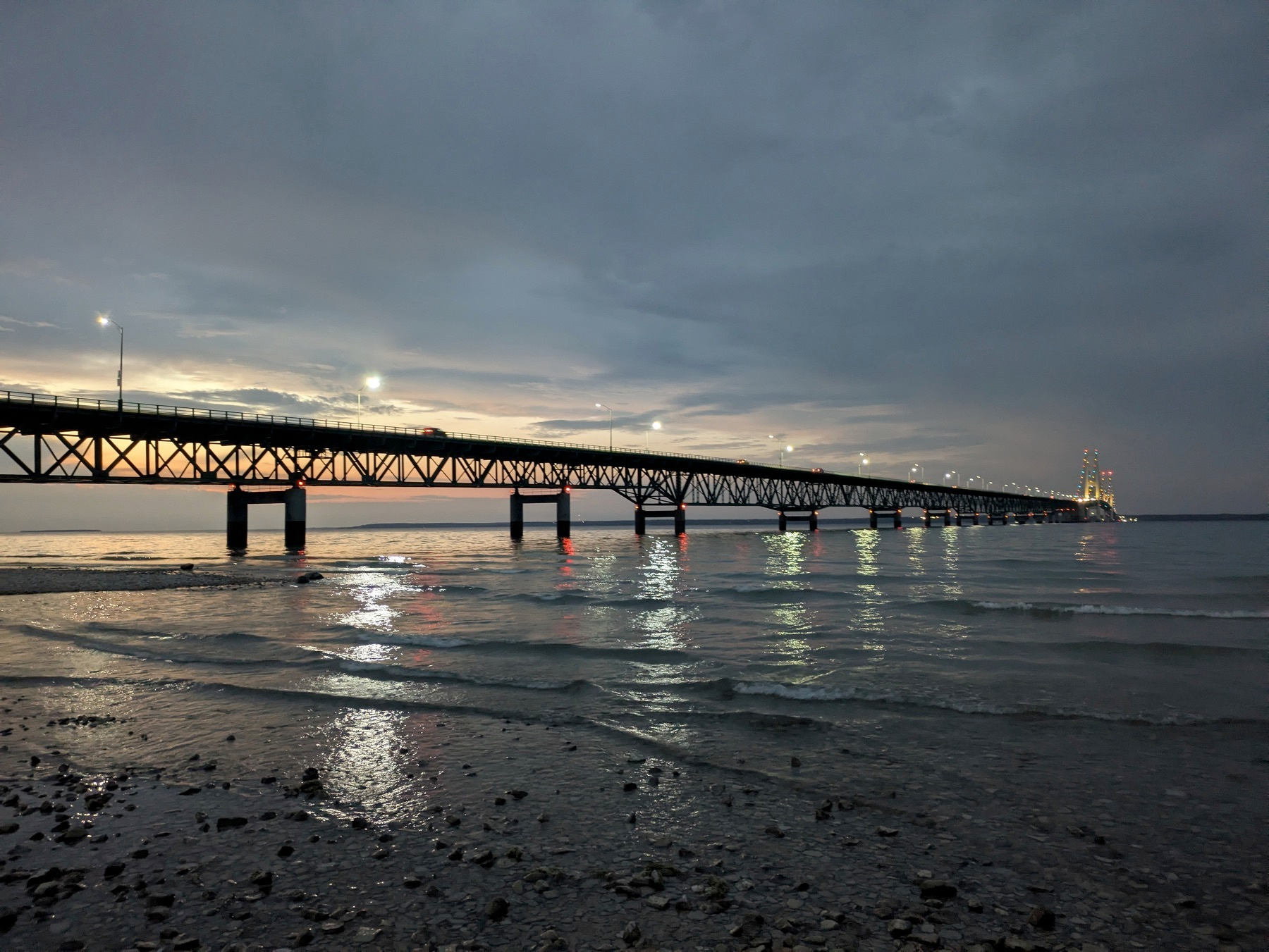 A long bridge stretches across a body of water under a cloudy, evening sky.