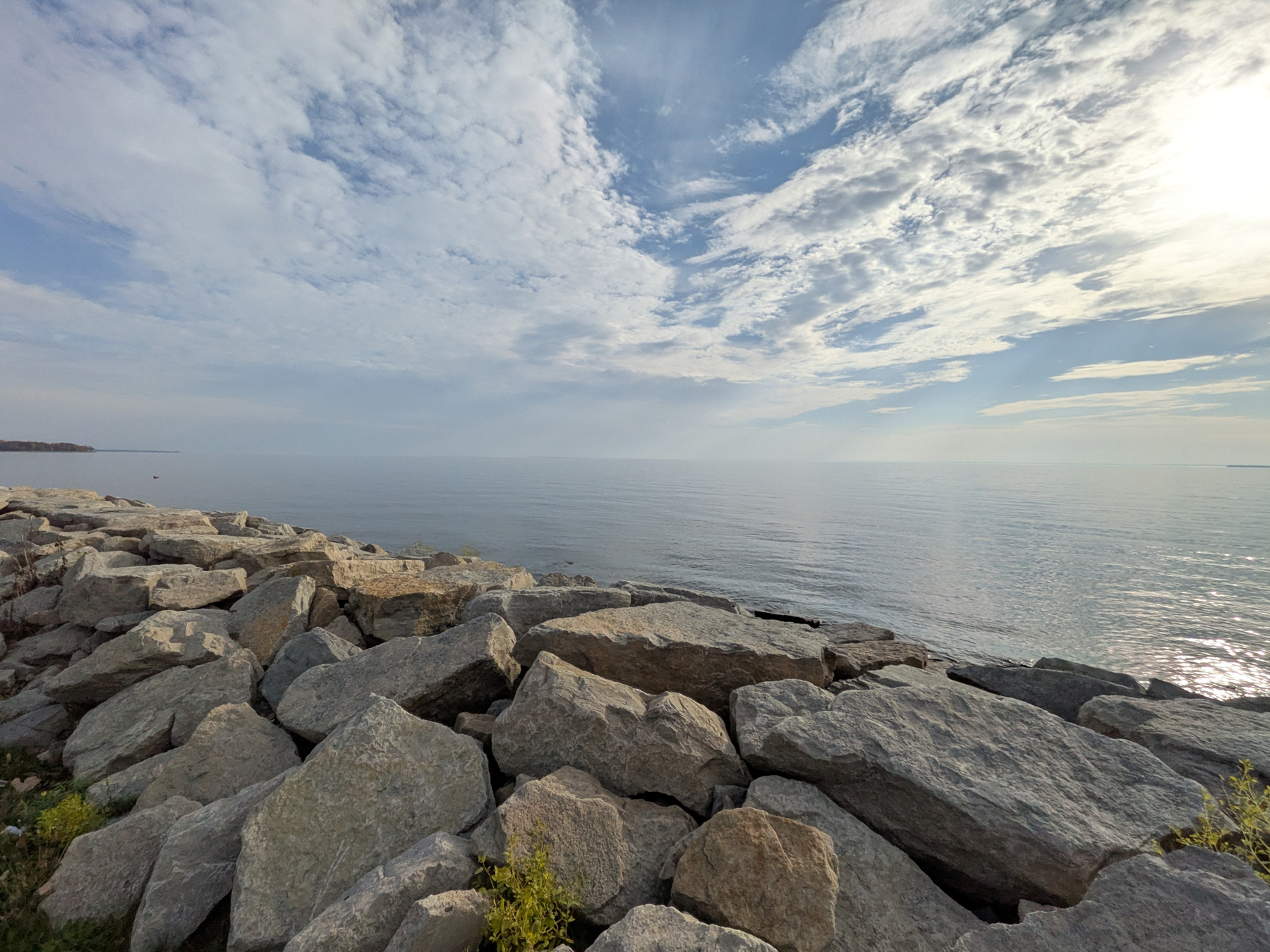 A rocky shoreline extends into a calm sea under a partly cloudy sky with sunlight breaking through.