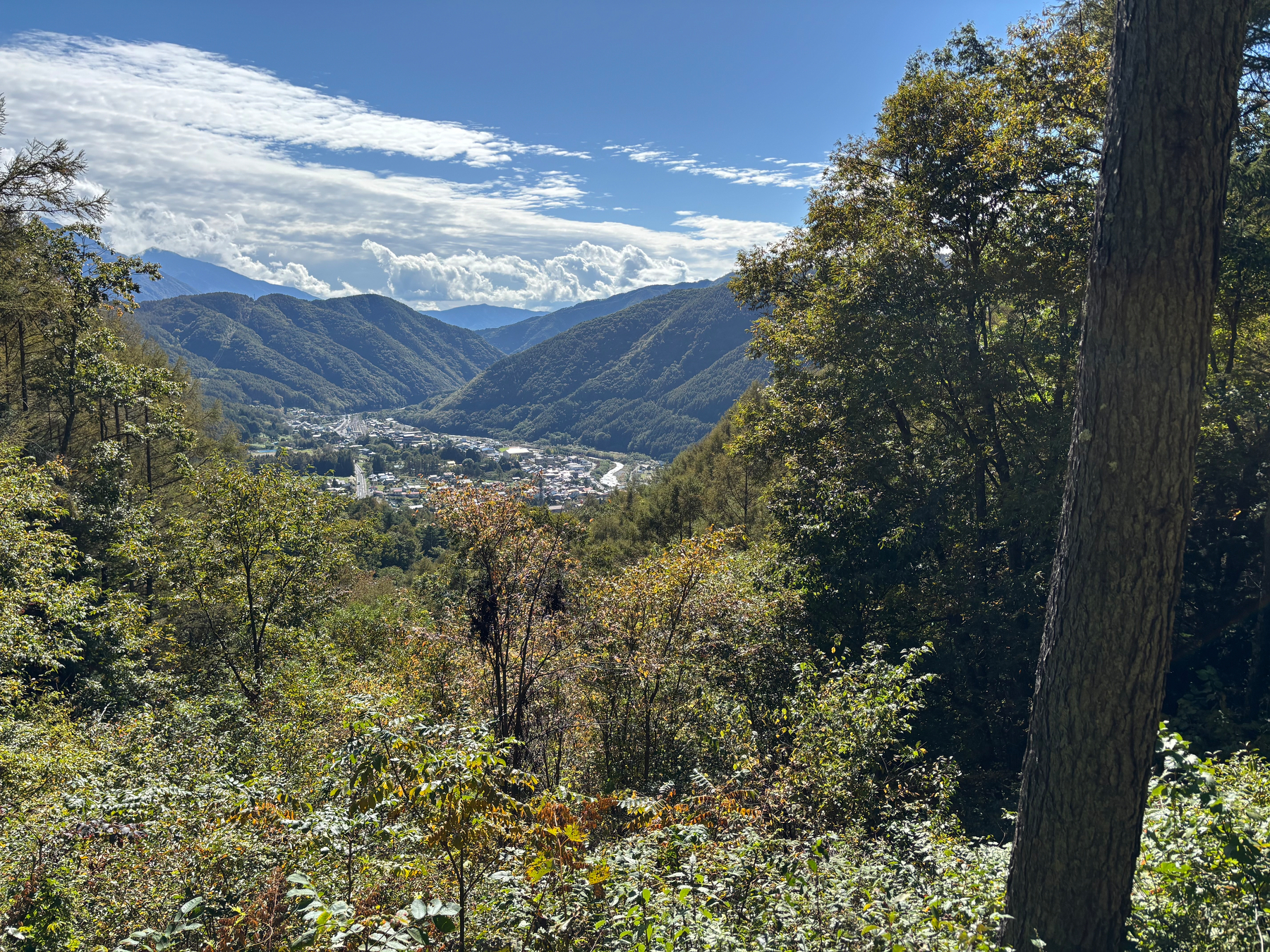 A scenic view of Yabuhara captures a lush, mountainous landscape with the town nestled between the hills under a clear blue sky.
