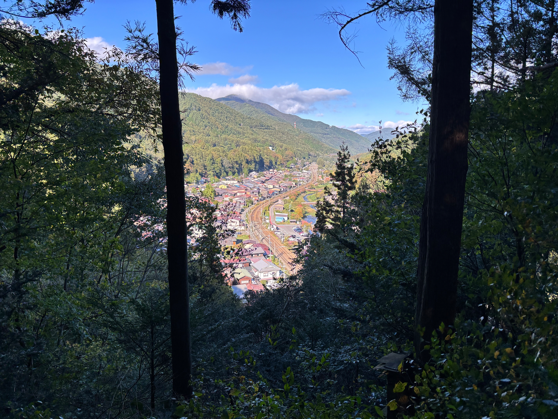 A picturesque view of Narai through a forest frames the town nestled in a valley surrounded by lush green hills.