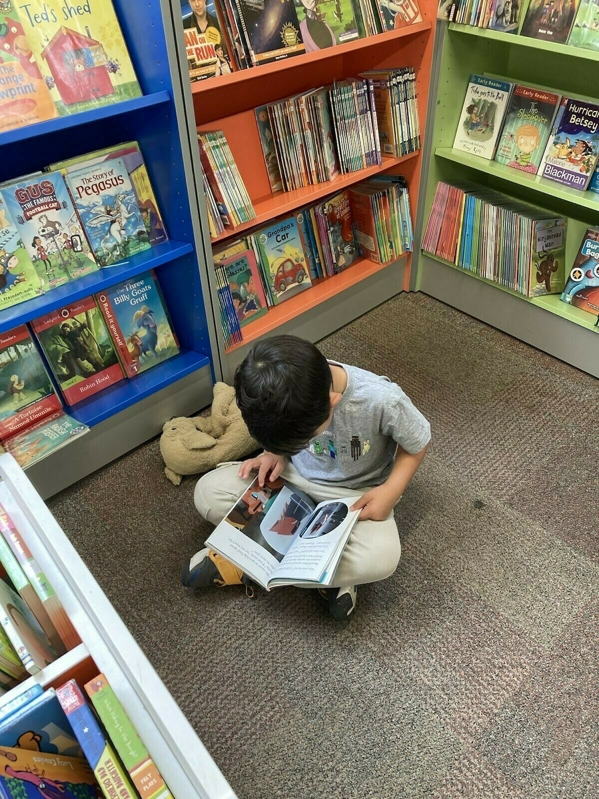 young boy sat on the floor reading a book in the library