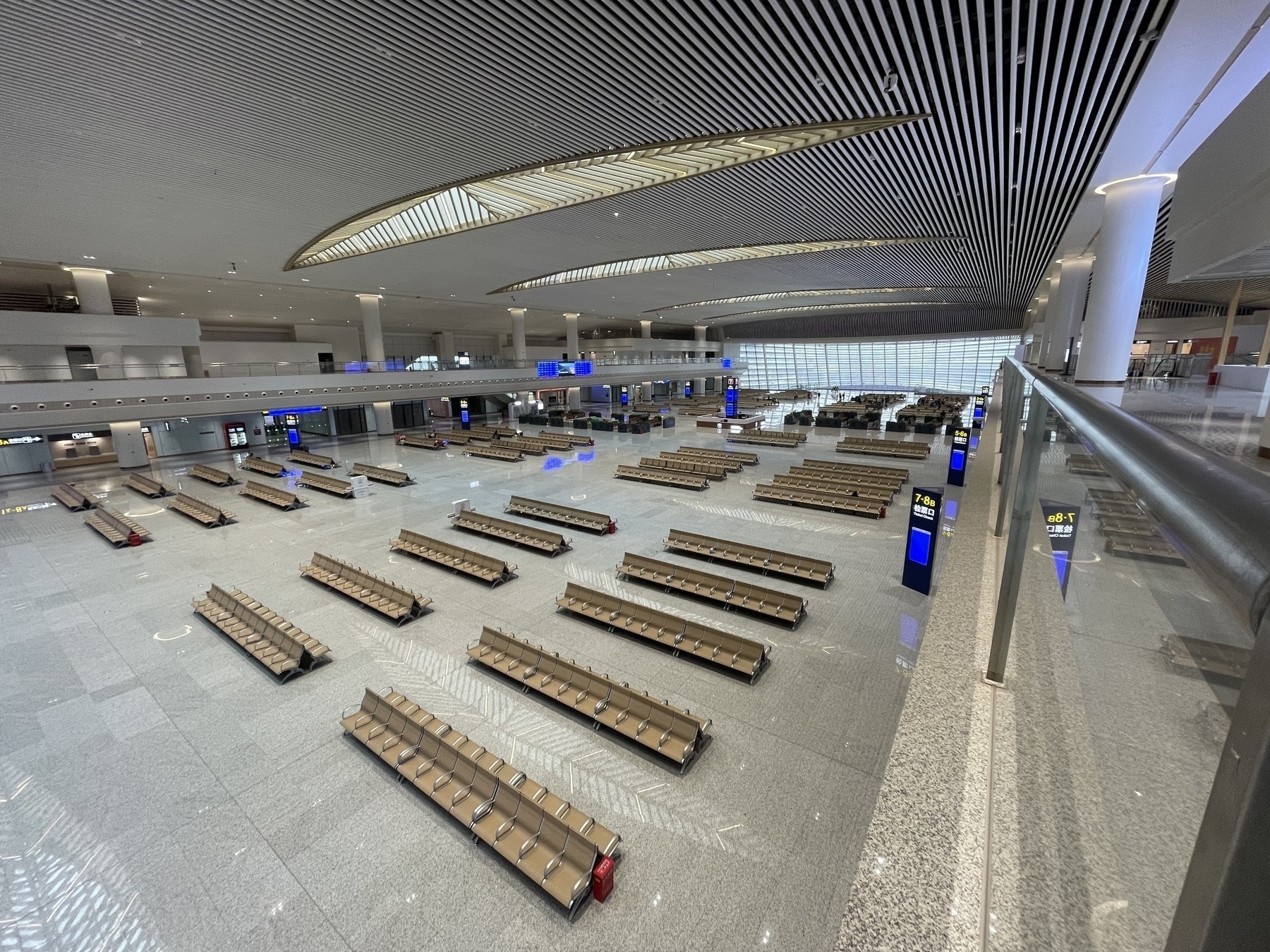 An expansive Chinese railway station features rows of empty seating areas under a high ceiling with modern lighting.