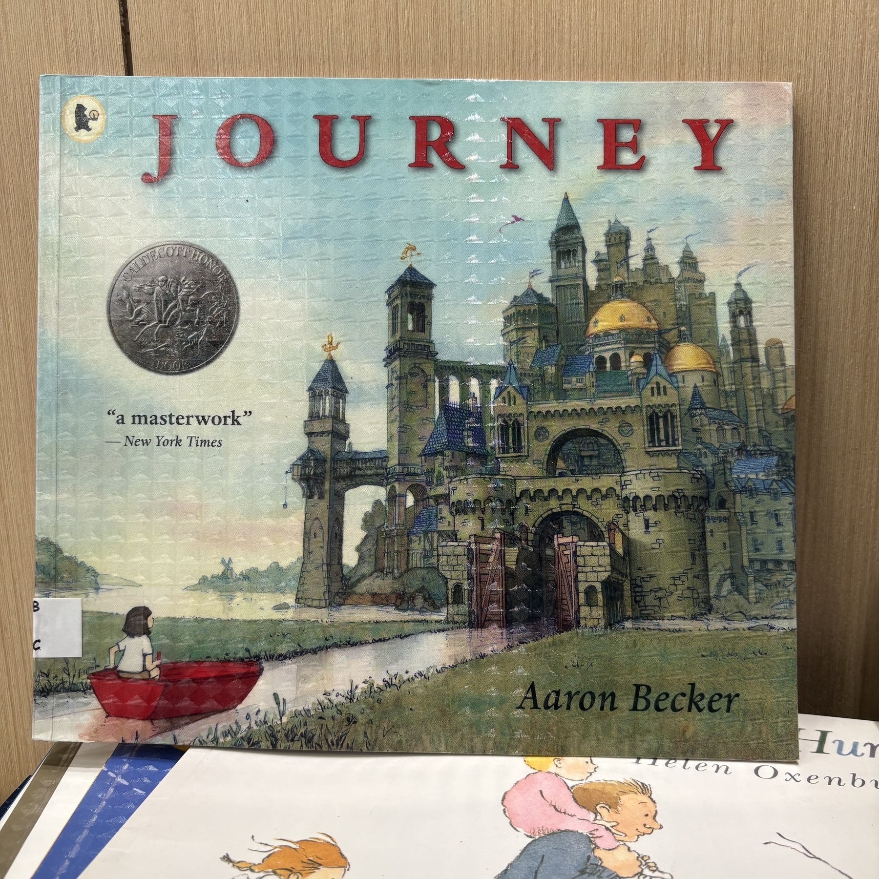 A children's book titled "Journey" by Aaron Becker features an illustrated castle and a girl with a red crayon on the cover.