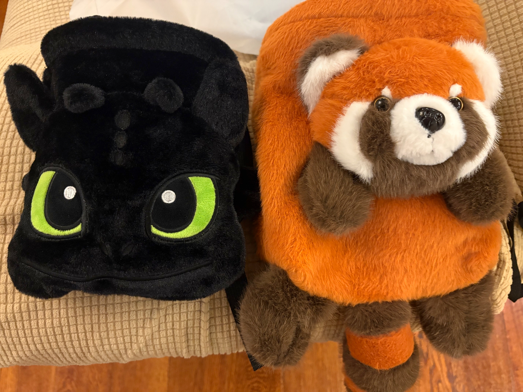 Two plush chalk bags, one resembling a black dragon (Toothless from How to train a dragon) and the other a red panda, are placed side by side on a textured surface.