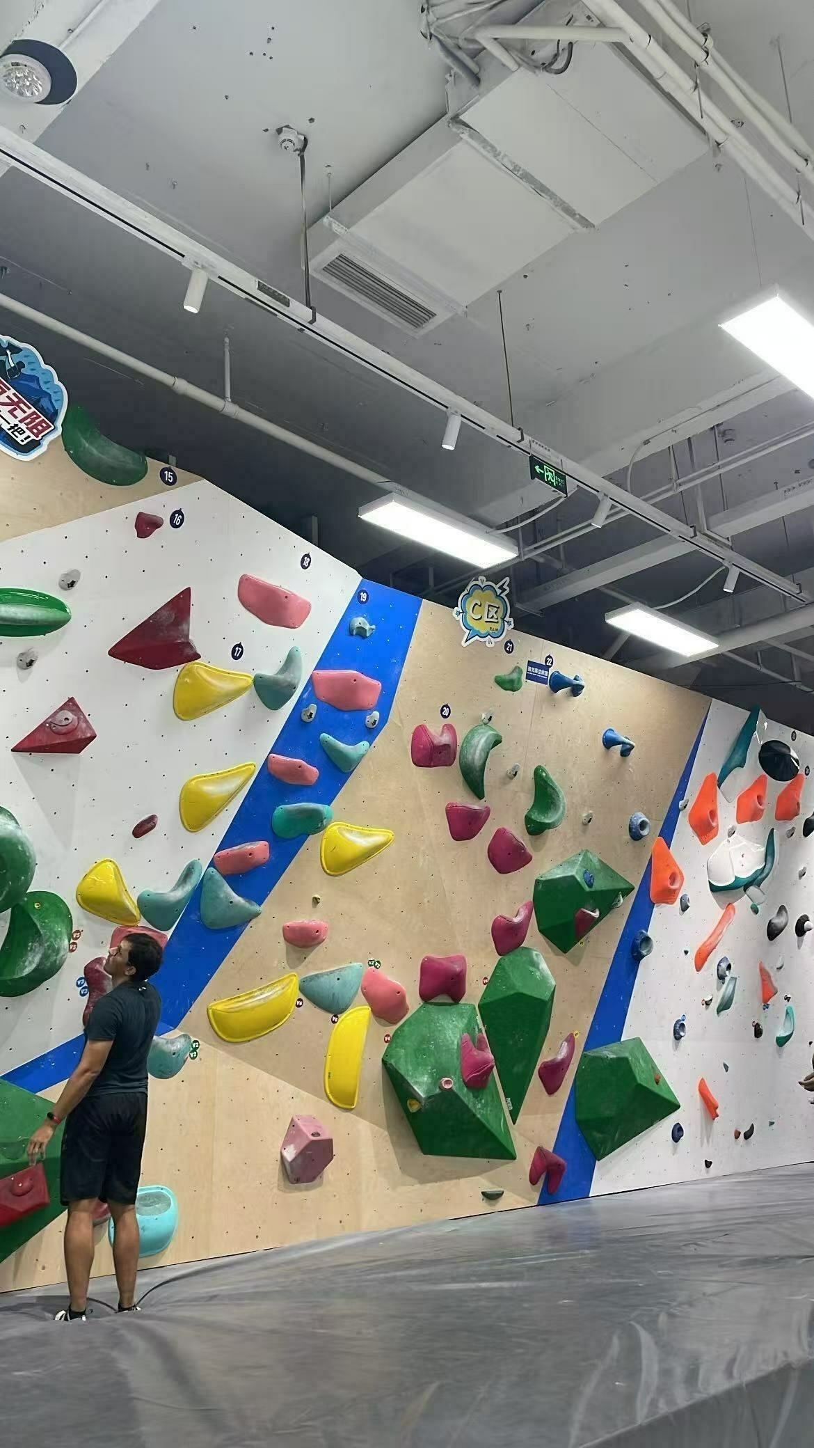 A person is observing a colourful indoor climbing wall with various handholds and footholds.