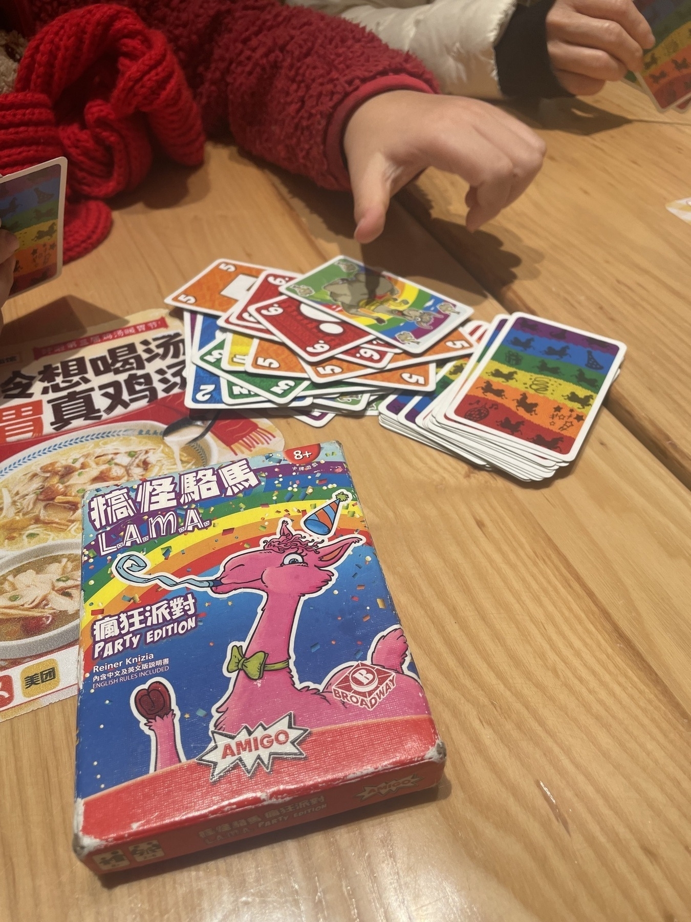 Several colorful playing cards are spread across a table next to a card game box with a llama illustration.