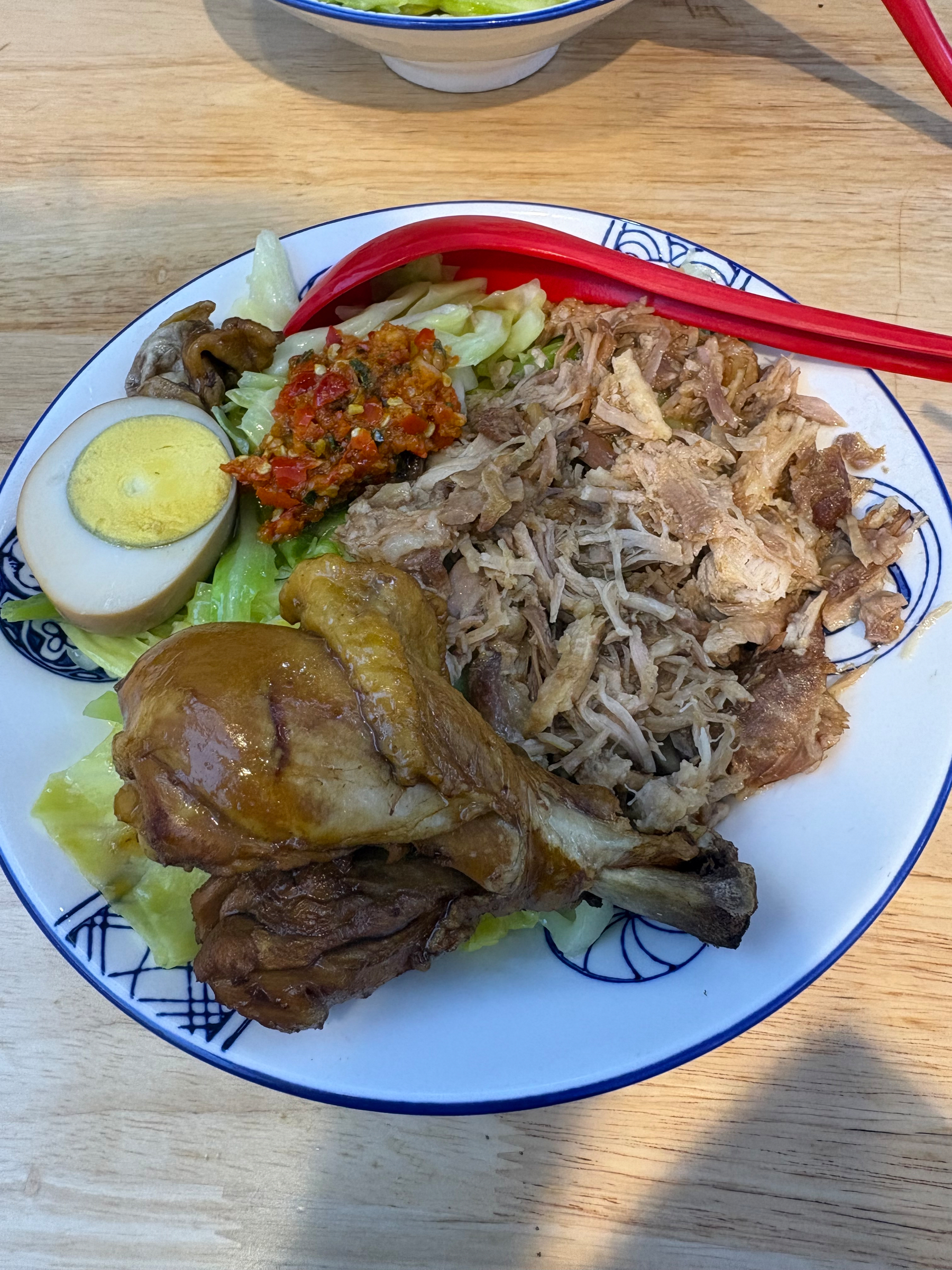 A plate of food featuring shredded meat, a cooked chicken drumstick, a halved boiled egg, lettuce, sambal chili sauce, and rice.