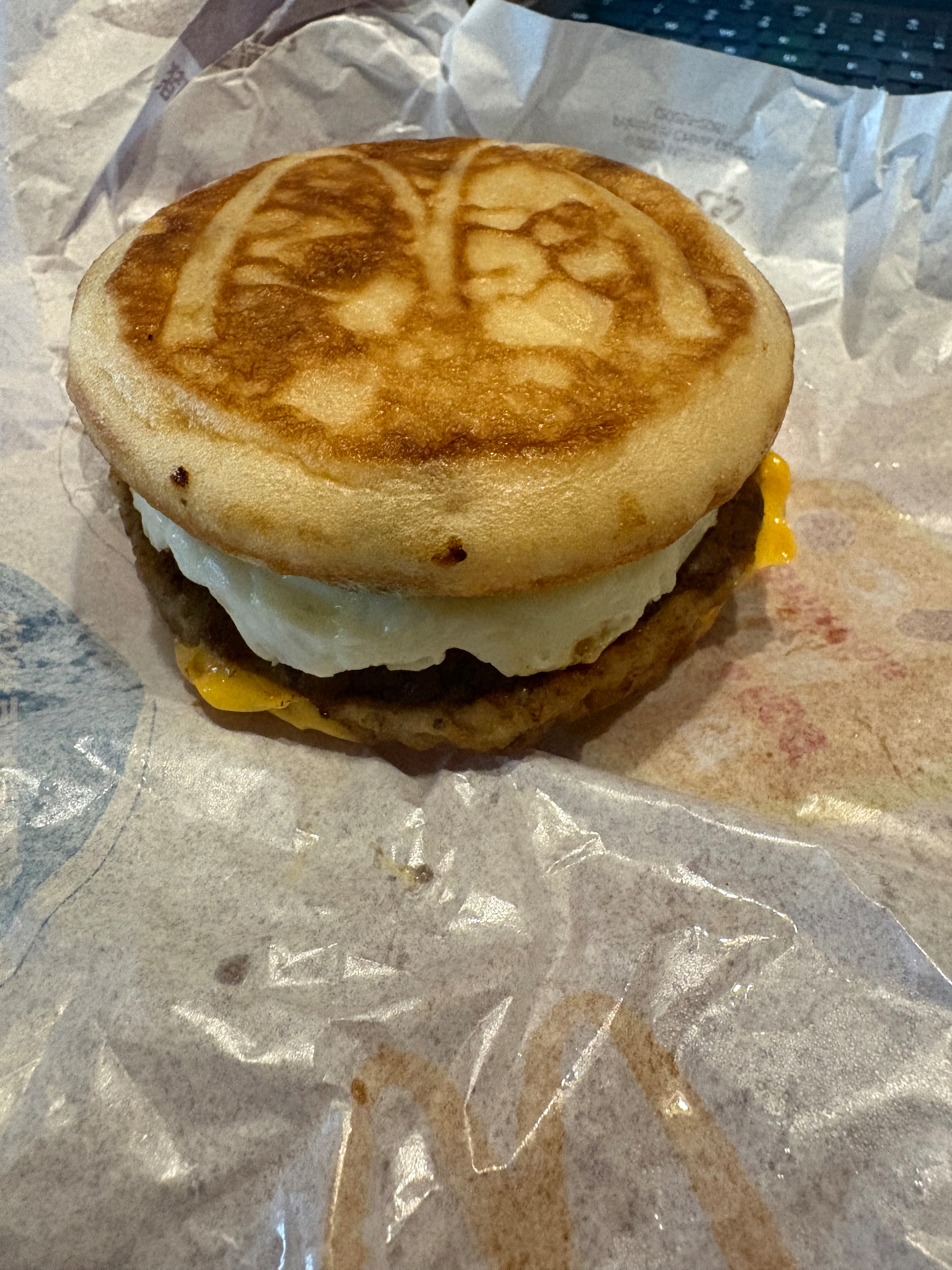 A breakfast sandwich with sausage, egg, and cheese is on a wrapper, featuring McDonald's logo on a waffle.