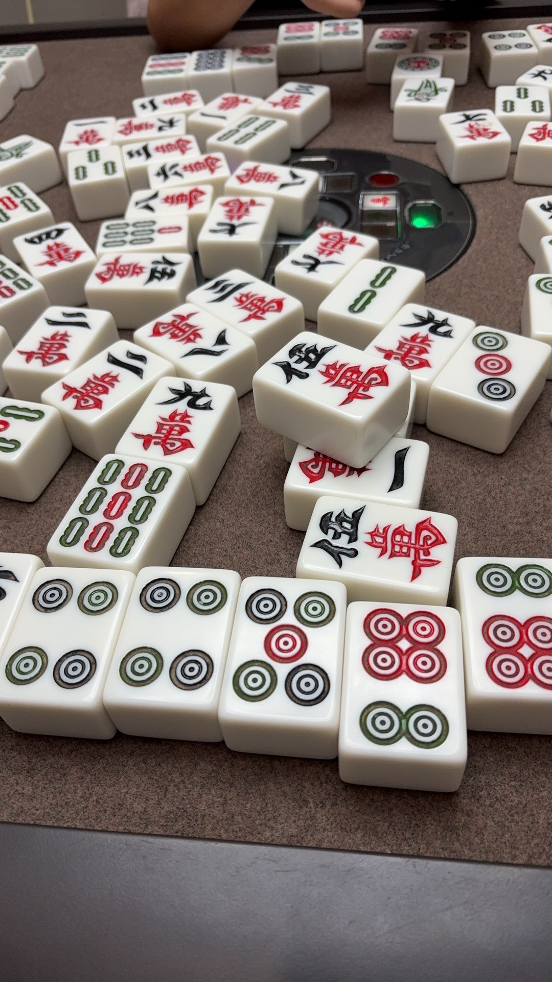 A game of mahjong is in progress with numerous tiles featuring circles, characters, and bamboo spread out on a table.