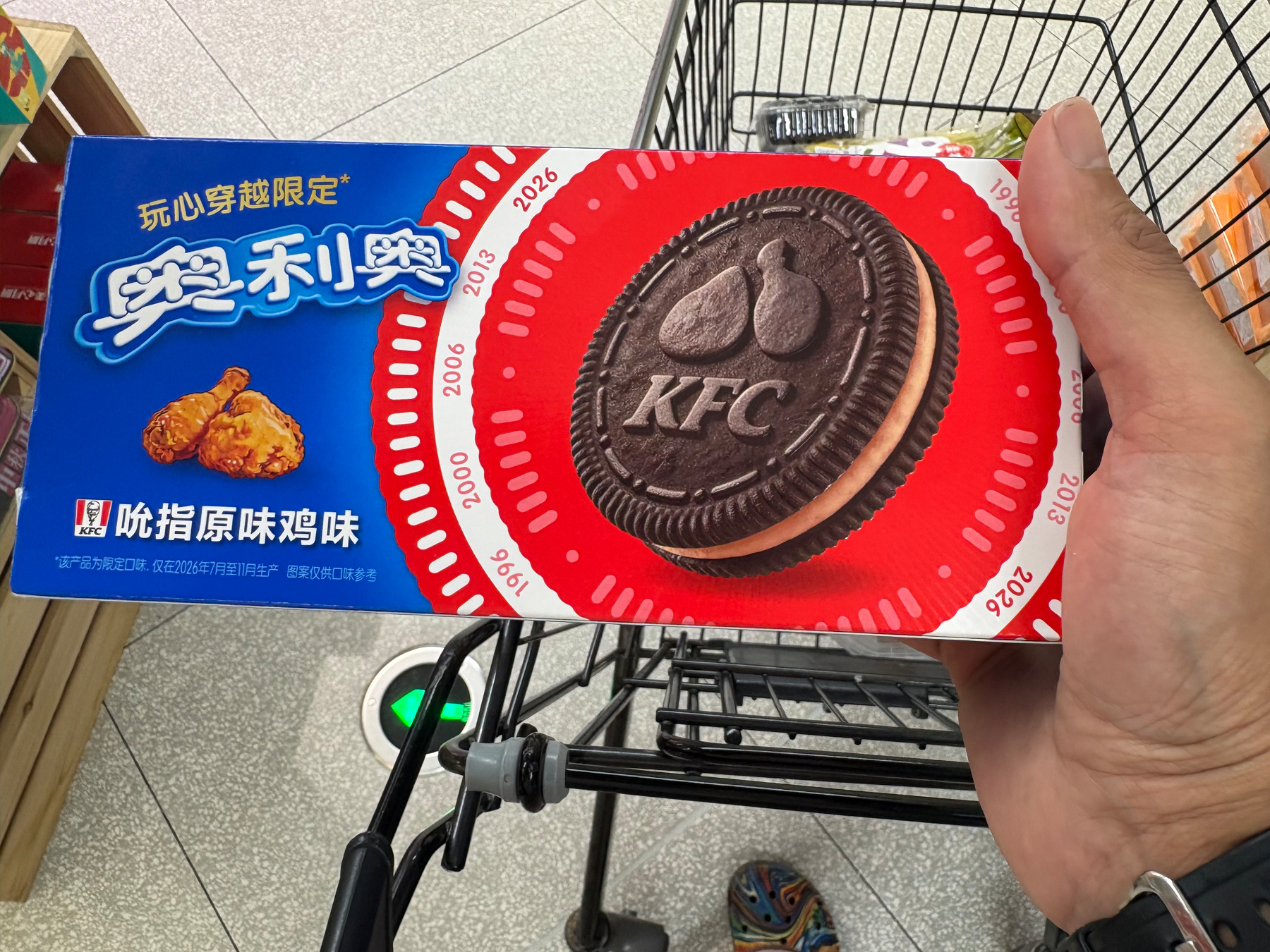 A hand is holding a box of KFC-themed cookies resembling Oreos, featuring fried chicken and the KFC logo on the packaging.