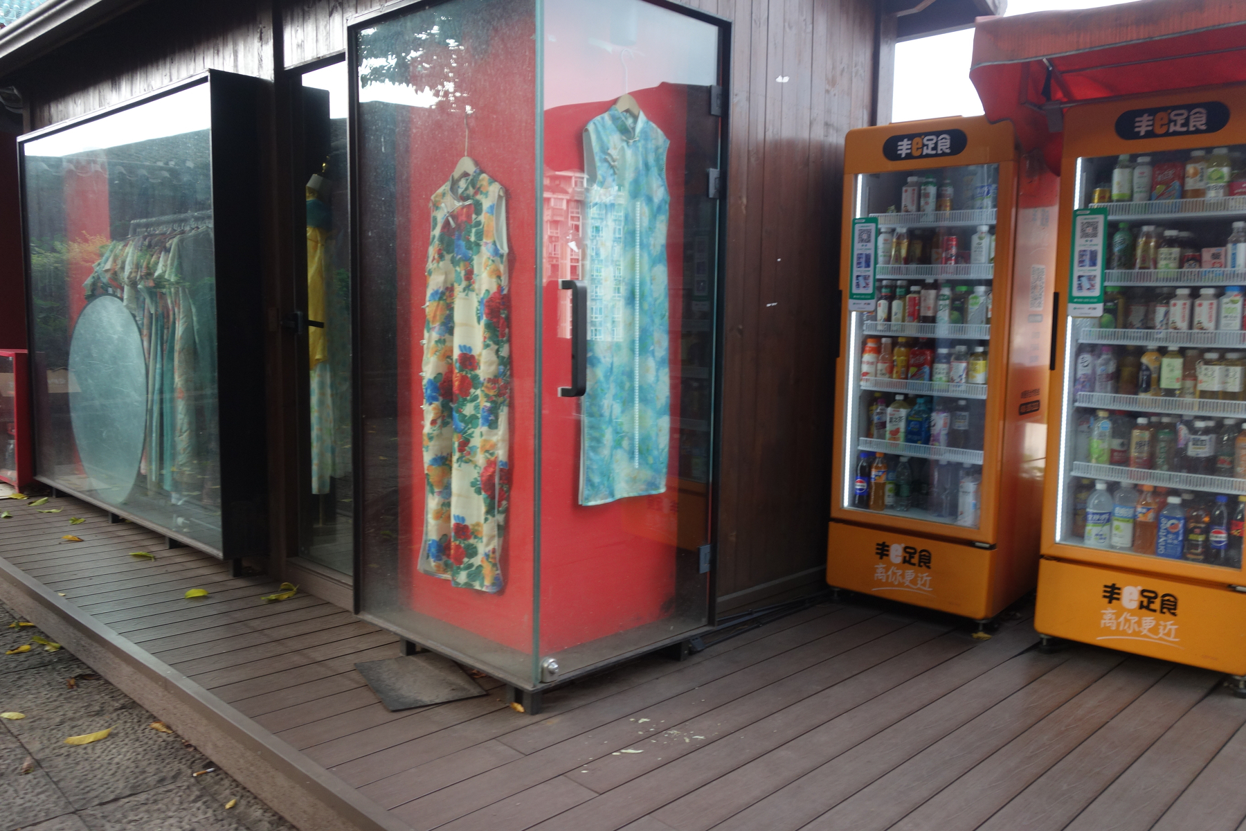 A display of traditional dresses is showcased in glass cases next to vending machines offering various beverages.