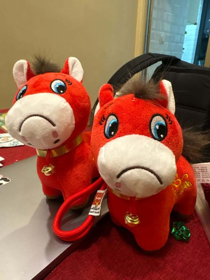 Two red horse plush toys with white faces and decorative bells are sitting on a table.