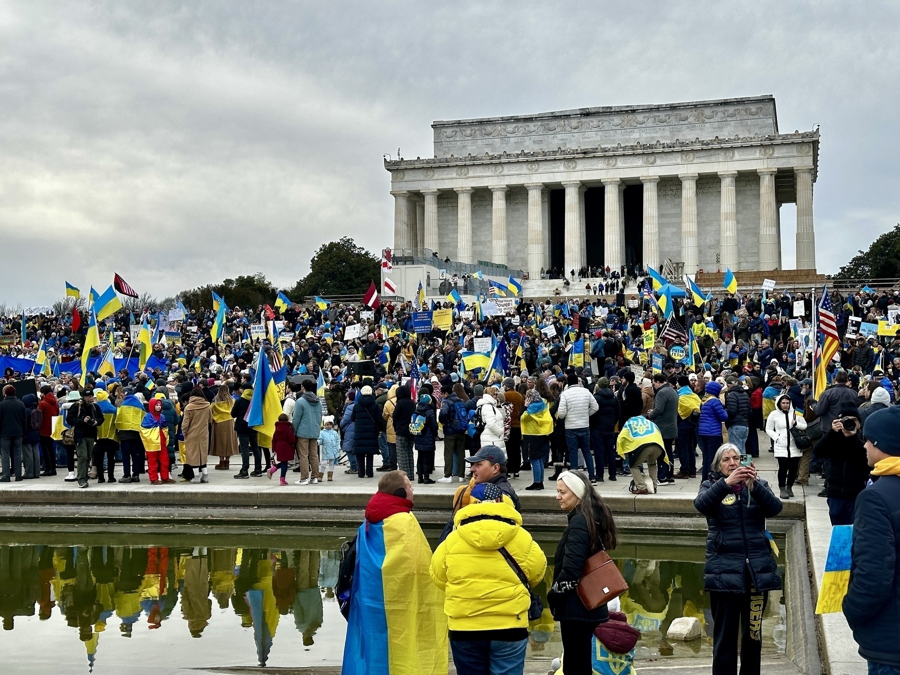 A large crowd with Ukrainian flags gathers in front of the Lincoln Memorial reflecting pool.