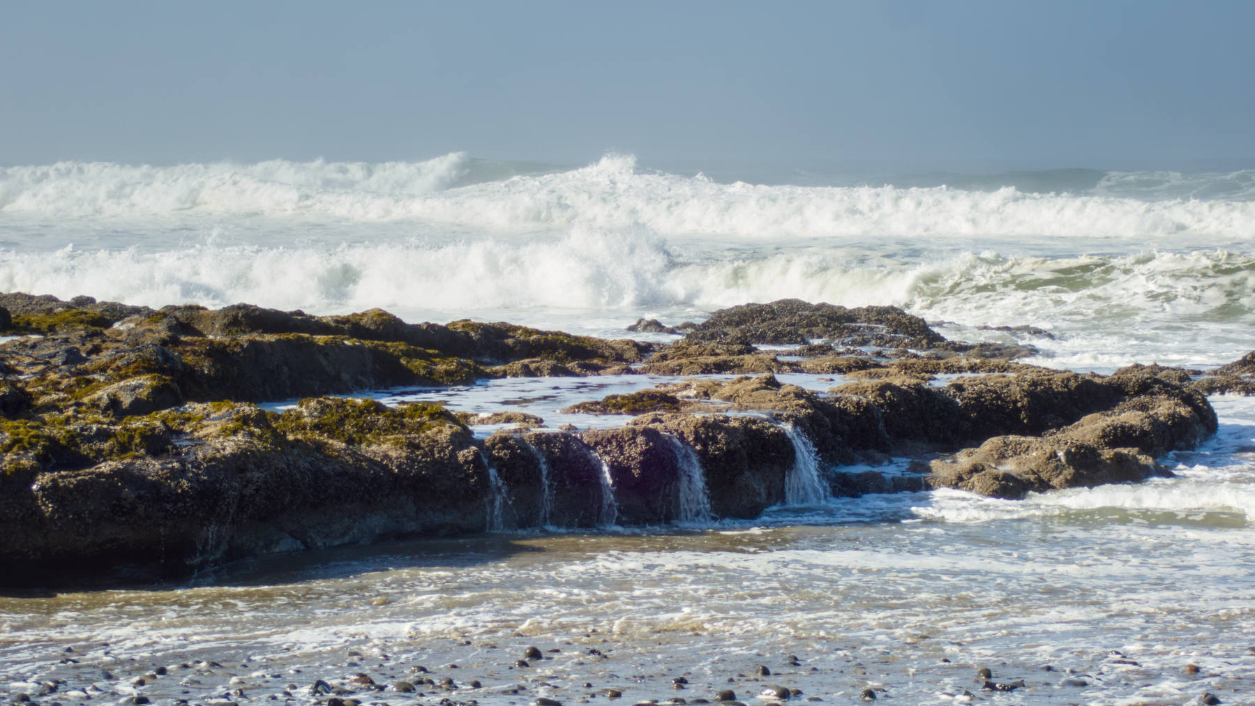 water pouring out of a tidepool with waves behind