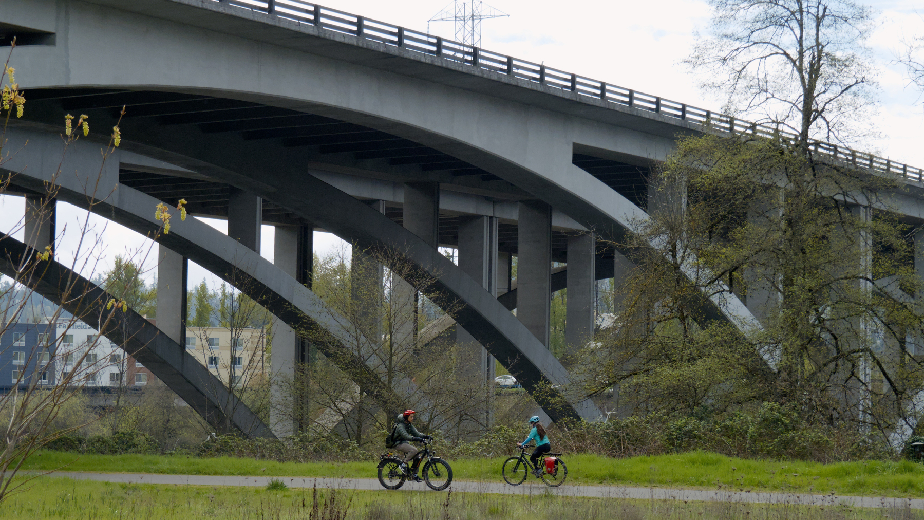 two bicyclists ride under a giant highway bridge