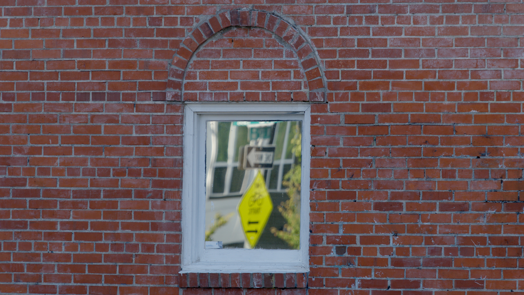 street sign reflected in a window in a brick wall