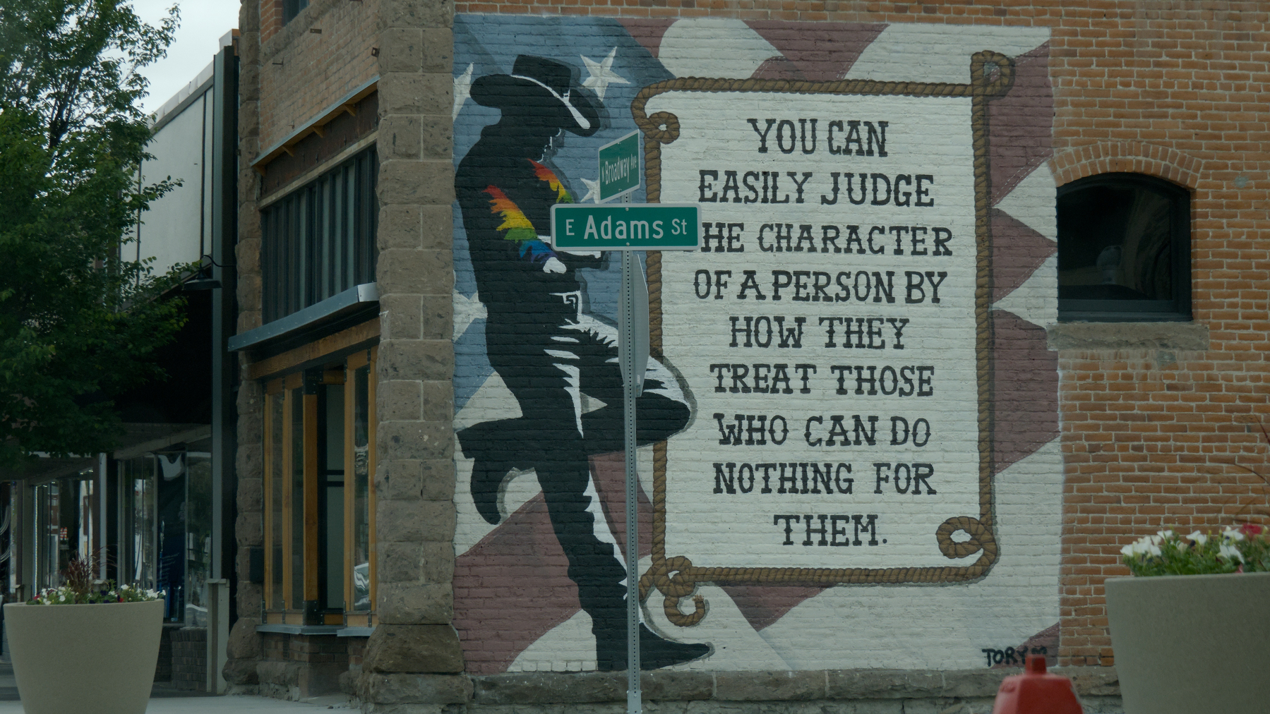 mural of a cowboy with rainbow-striped sleeves on a brick wall