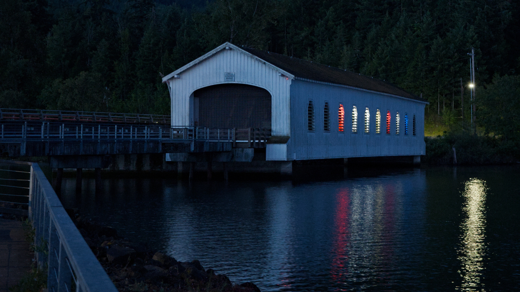 covered bridge lighted from inside and reflected in the lake