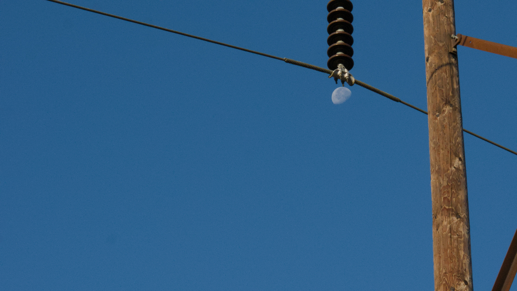 insulator on a power pole reaches down to (apparently) grab the moon out of the sky