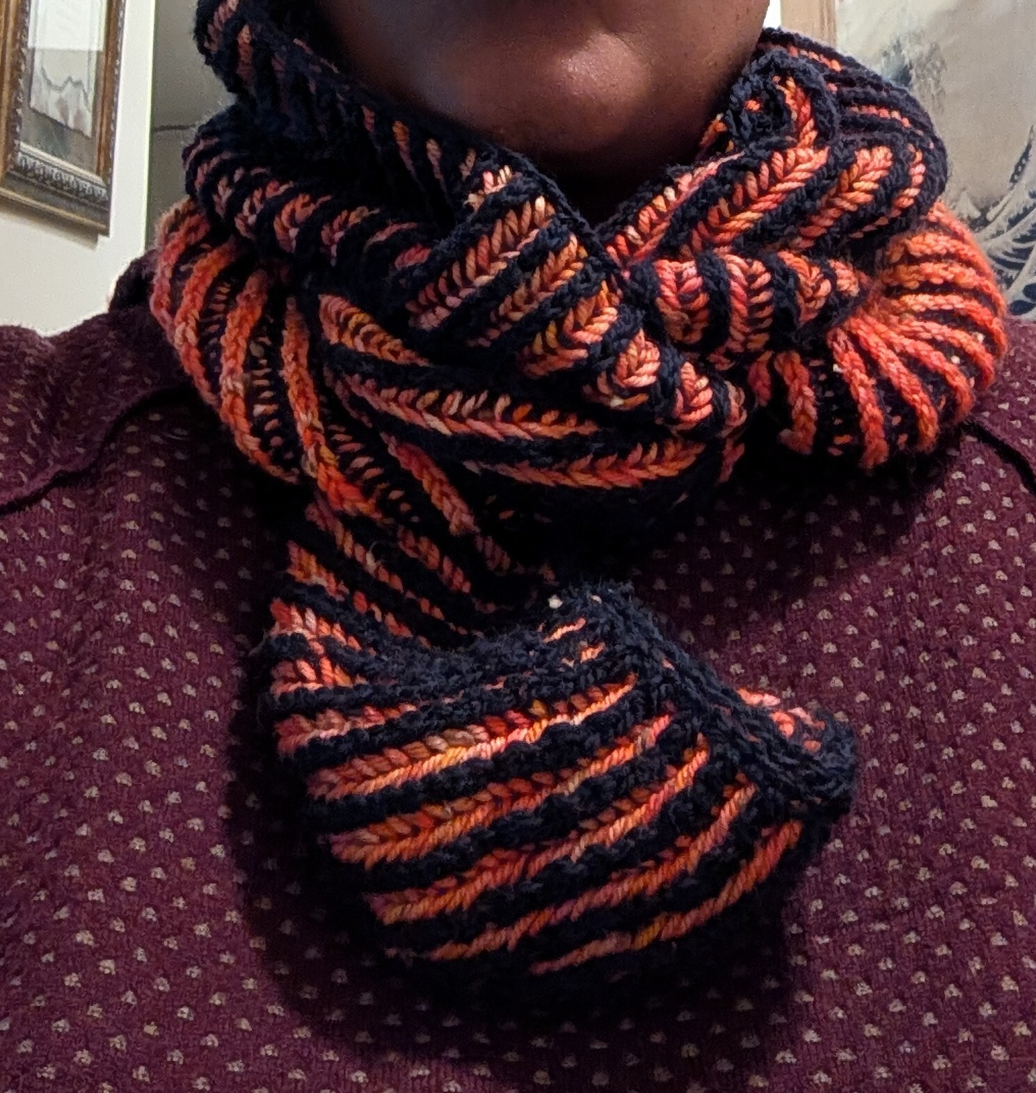 A person is wearing a thick knitted scarf with alternating orange and dark blue stripes wrapped around their neck.