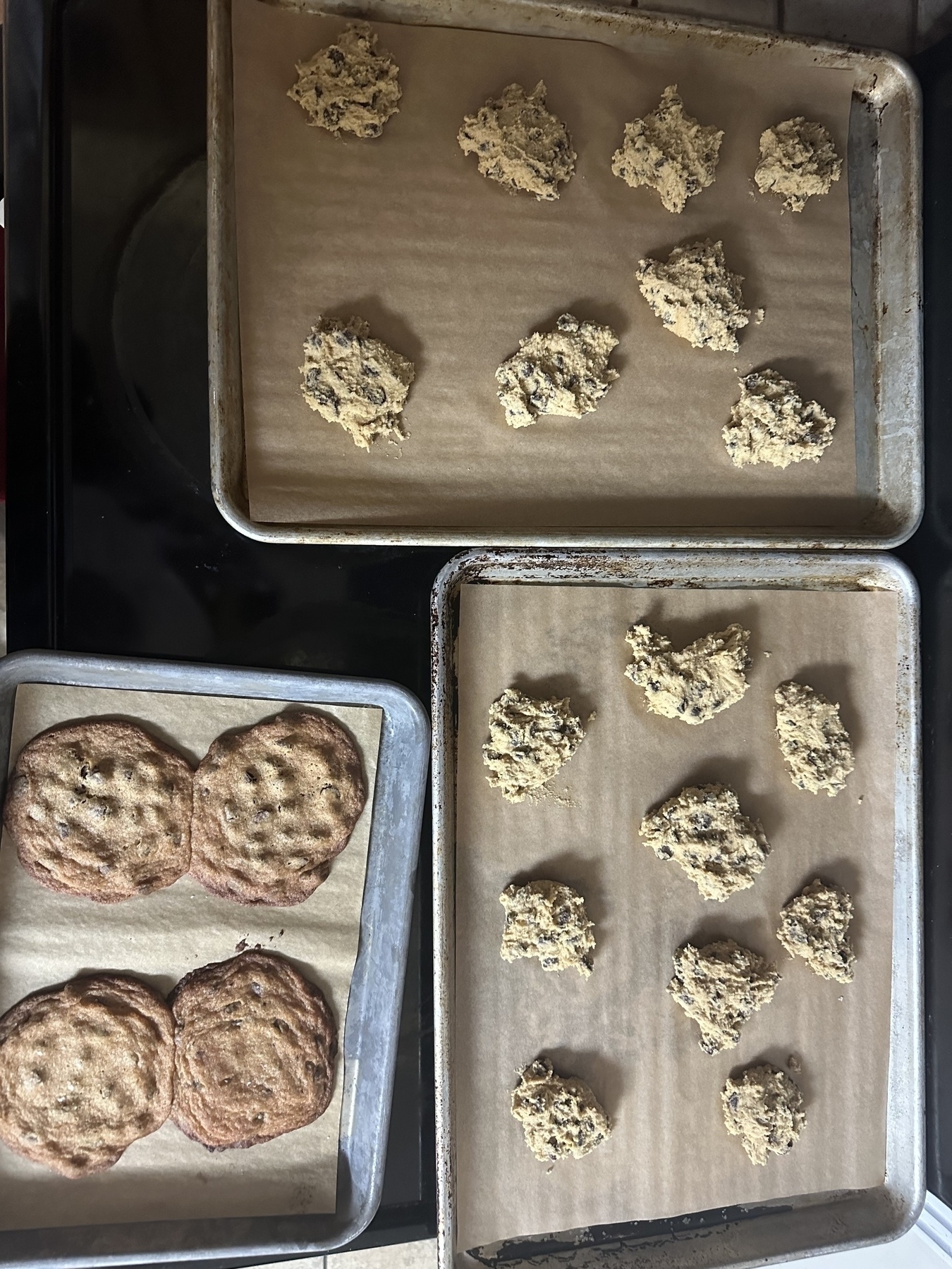 A small tray of baked chocolate chip cookies and two larger trays on uncooked dough