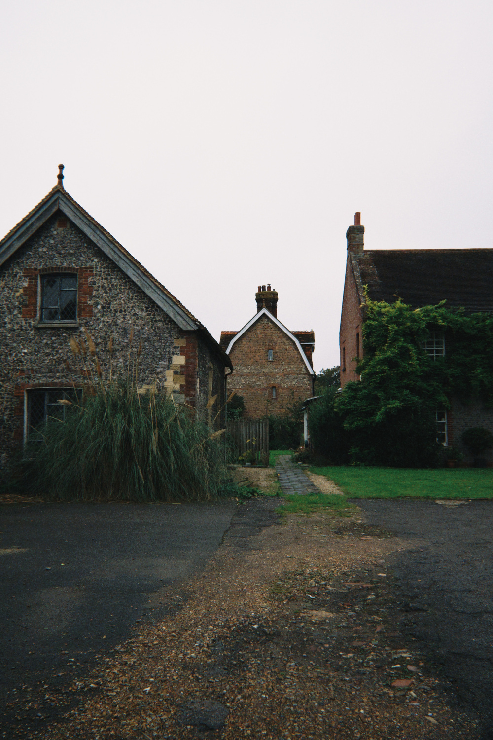 A rustic scene features three old stone buildings with pitched roofs, surrounded by a grassy area and a narrow path.