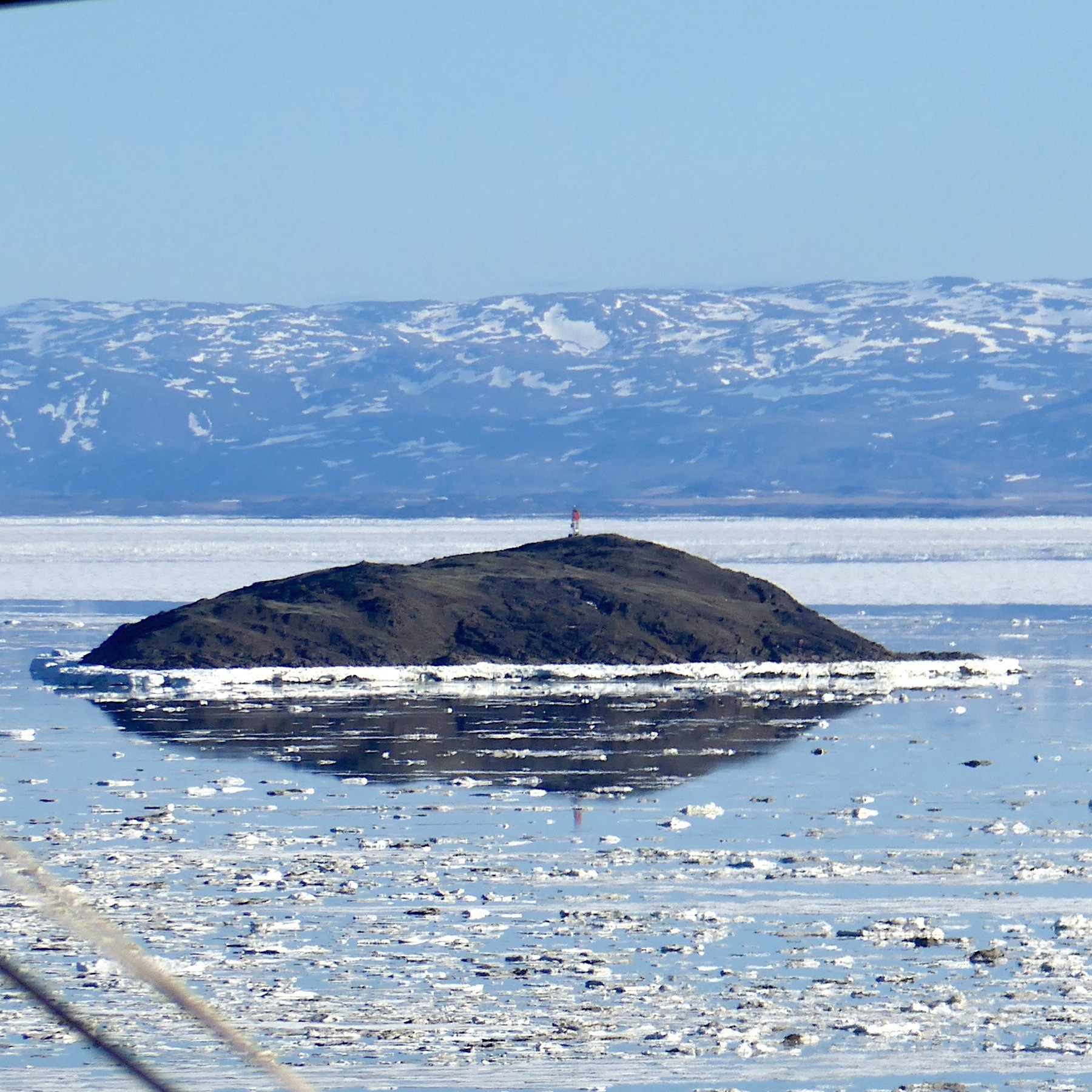 Island in the sea ice, surrounded by reflecting water on the surface; June 18, 2019