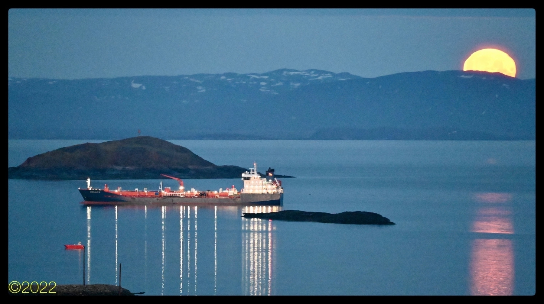 The cargo ship Qikigtaaluk W anchored in the night in Frobisher Bay, the moon dipping below the horizon to the right