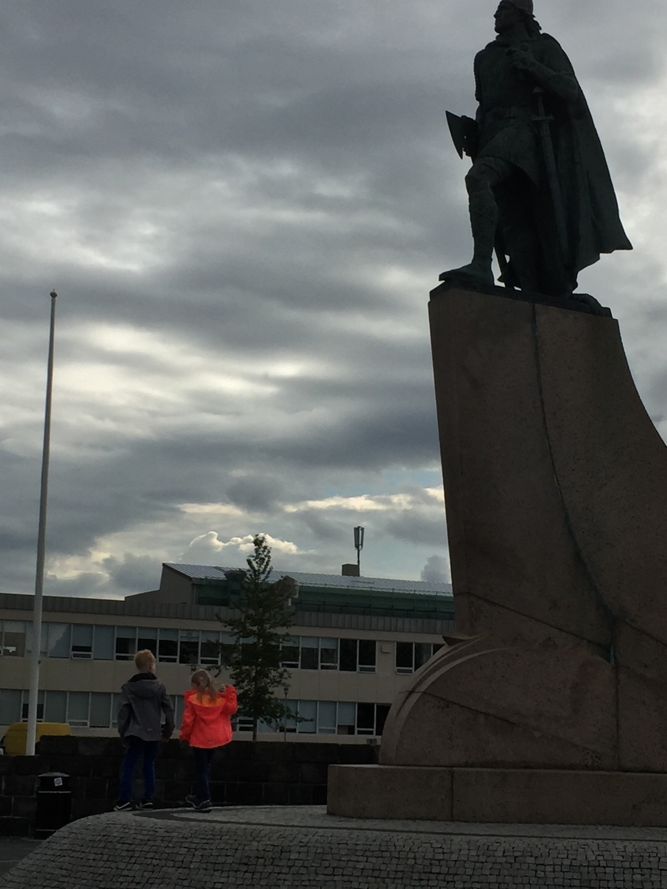 Statue in Reykjavik with two children in the foreground.  One is in a brightly covered jacket which stands out in an an otherwise largely monochrome picture.